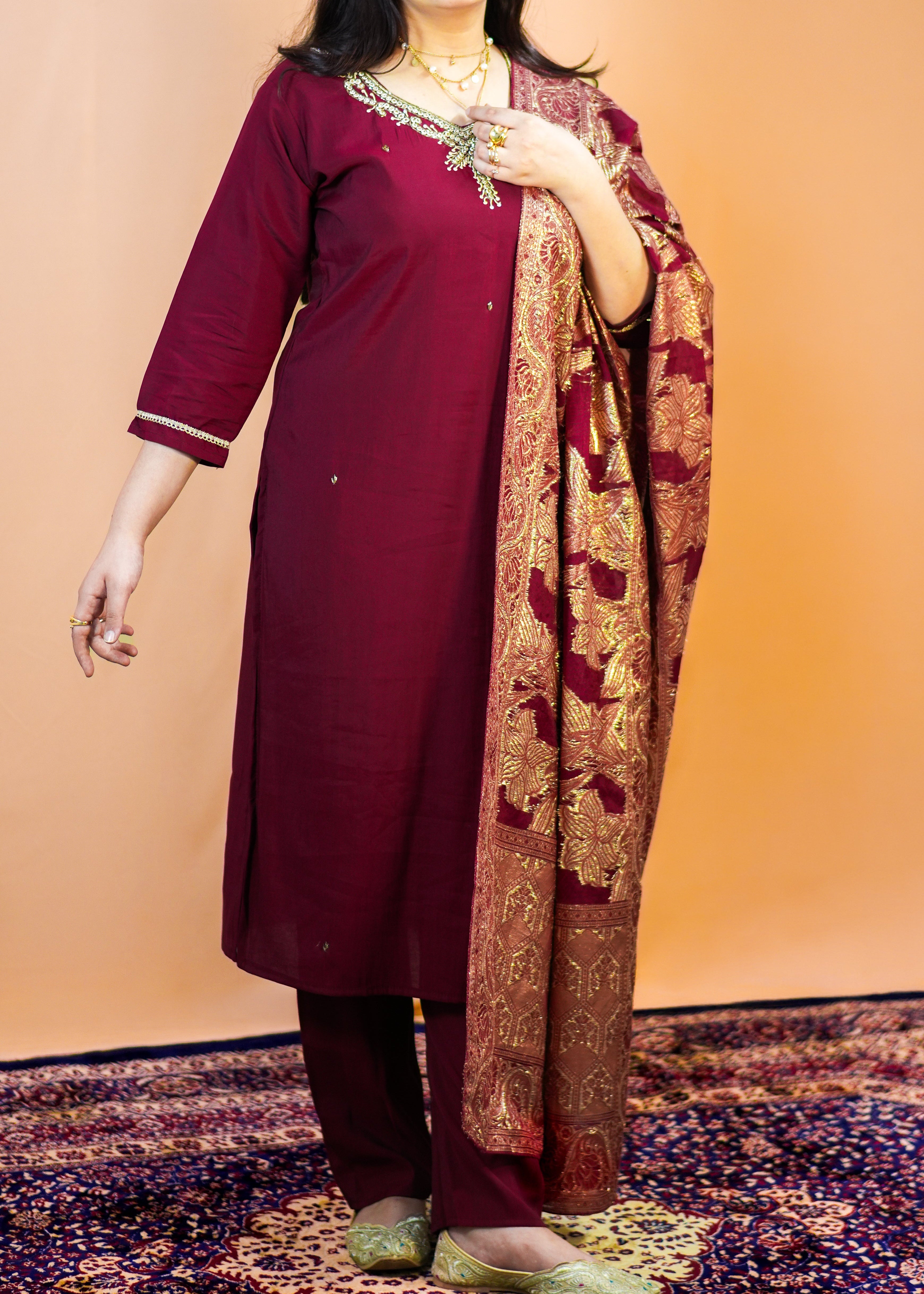 Woman in a maroon traditional outfit with a patterned scarf against an orange background