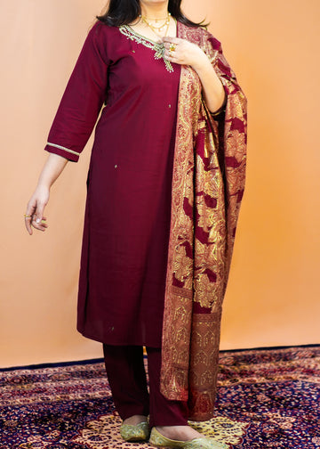 Woman in a maroon traditional outfit with a patterned scarf against an orange background