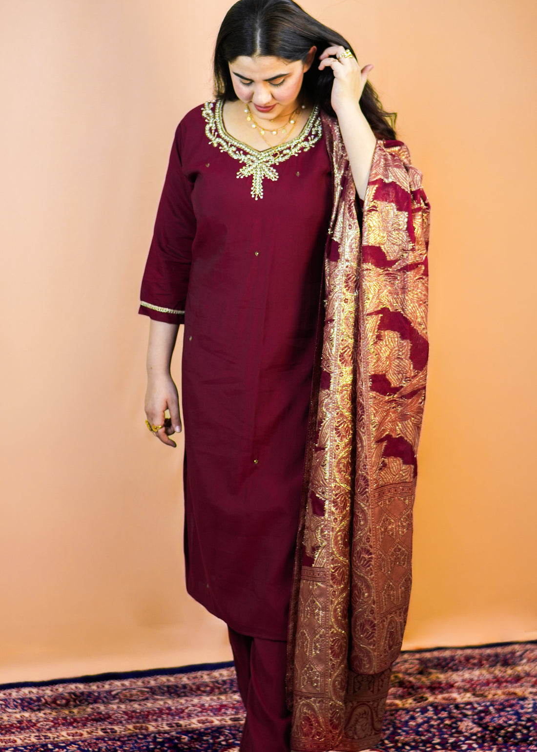 Woman in a maroon traditional outfit with a patterned scarf against an orange background