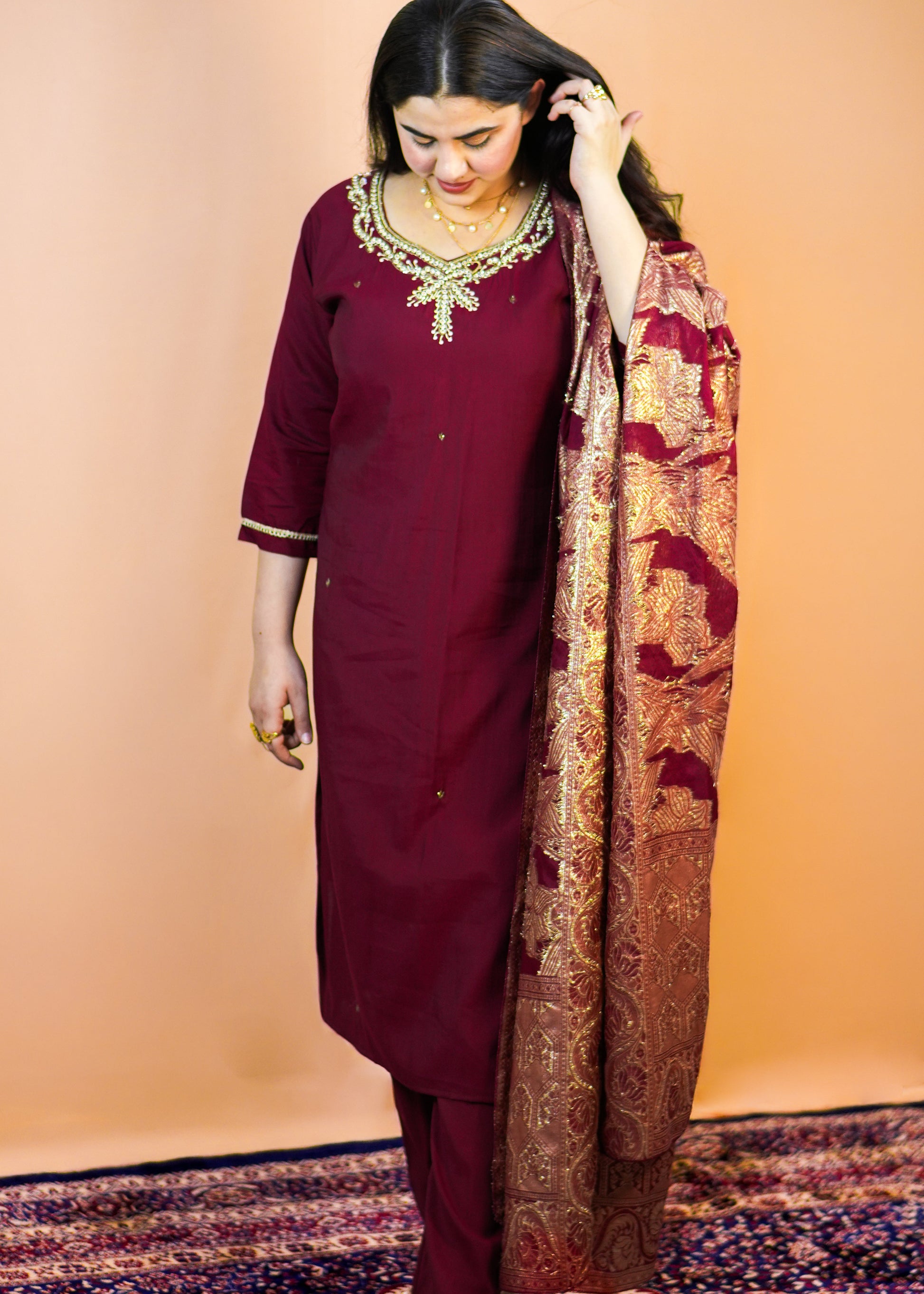 Woman in a maroon traditional outfit with a patterned shawl on a beige background