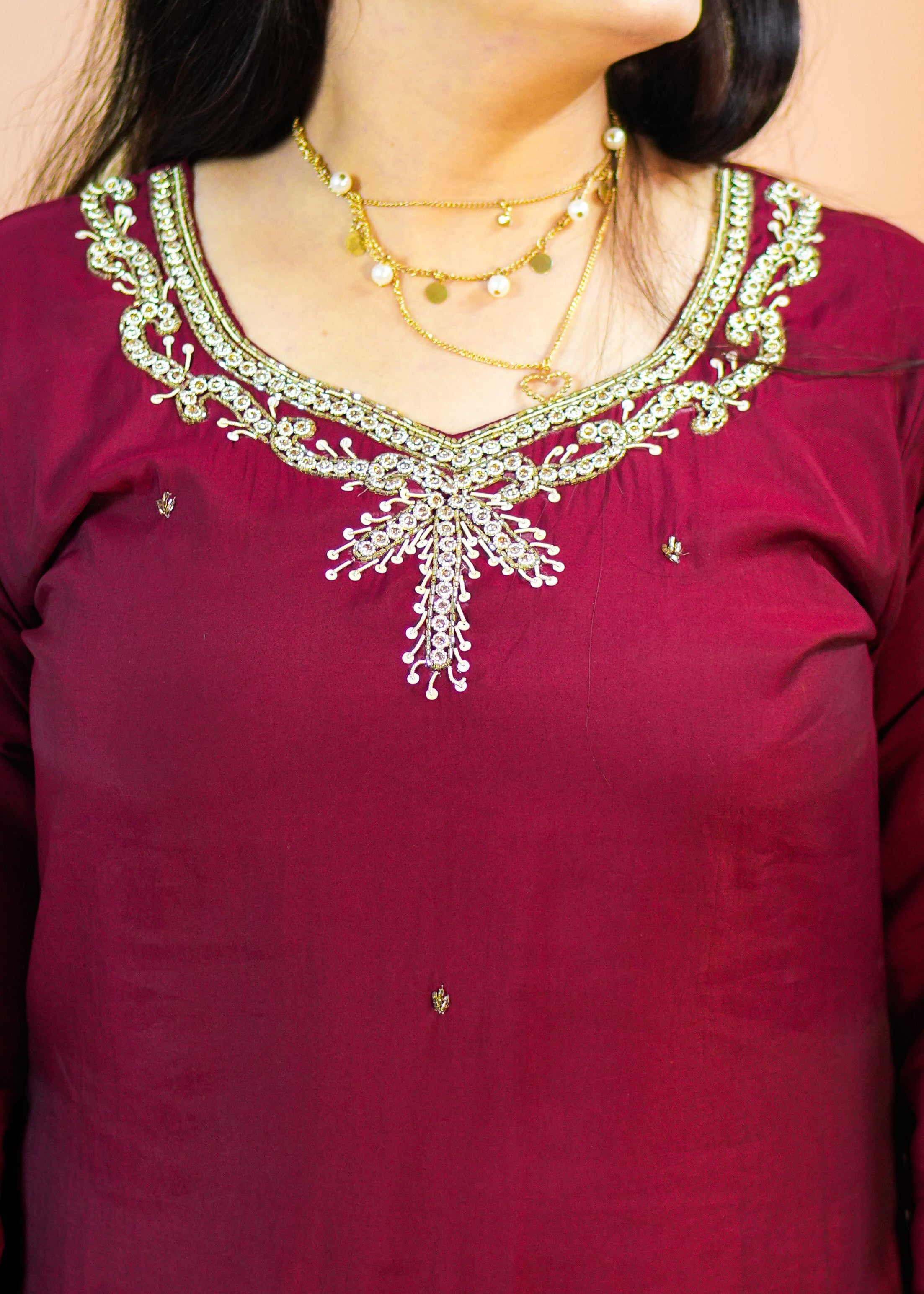 Woman wearing a maroon traditional outfit with gold embroidery against a beige background