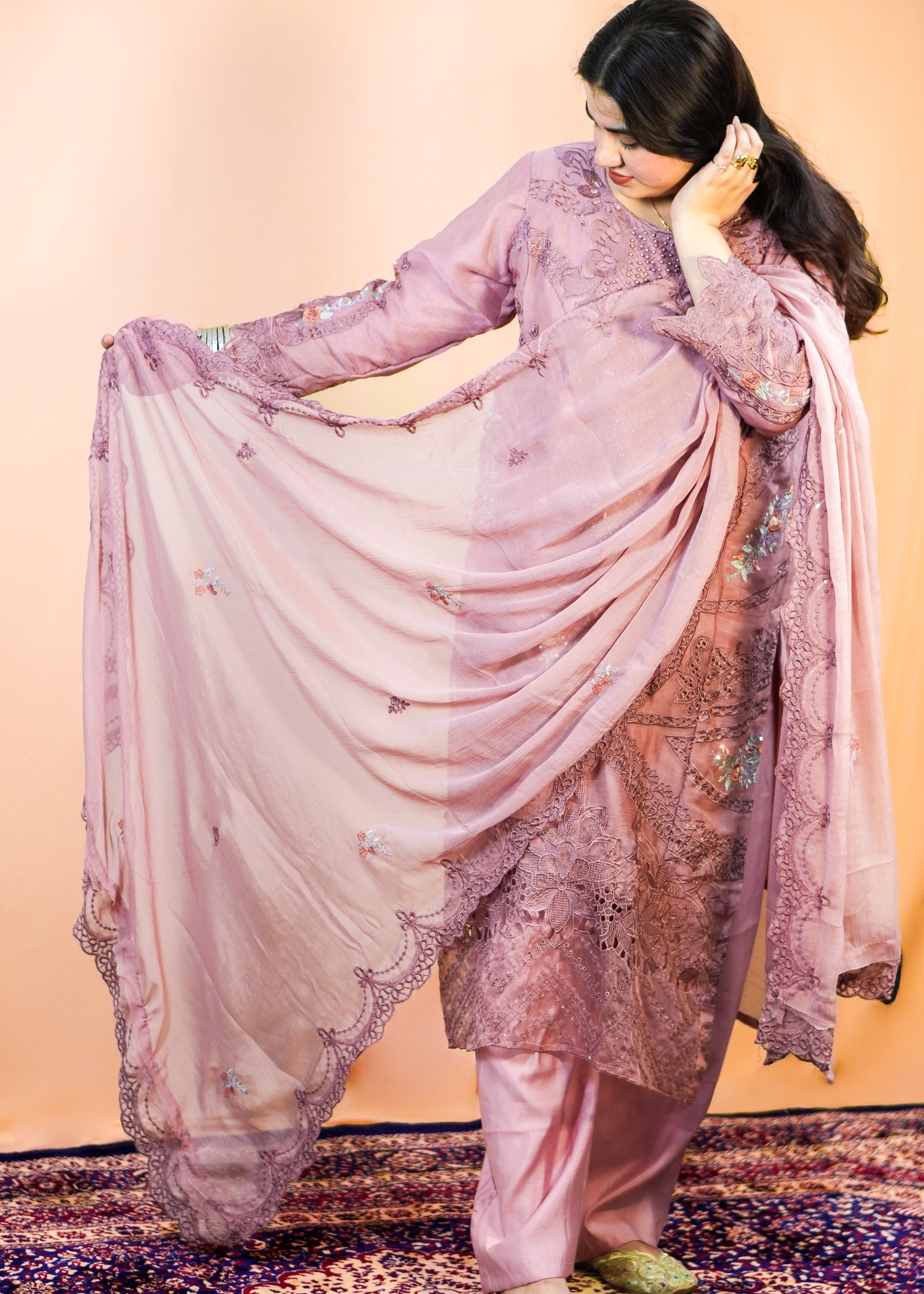 Woman in a pink traditional outfit with a floral pattern on a patterned rug.
