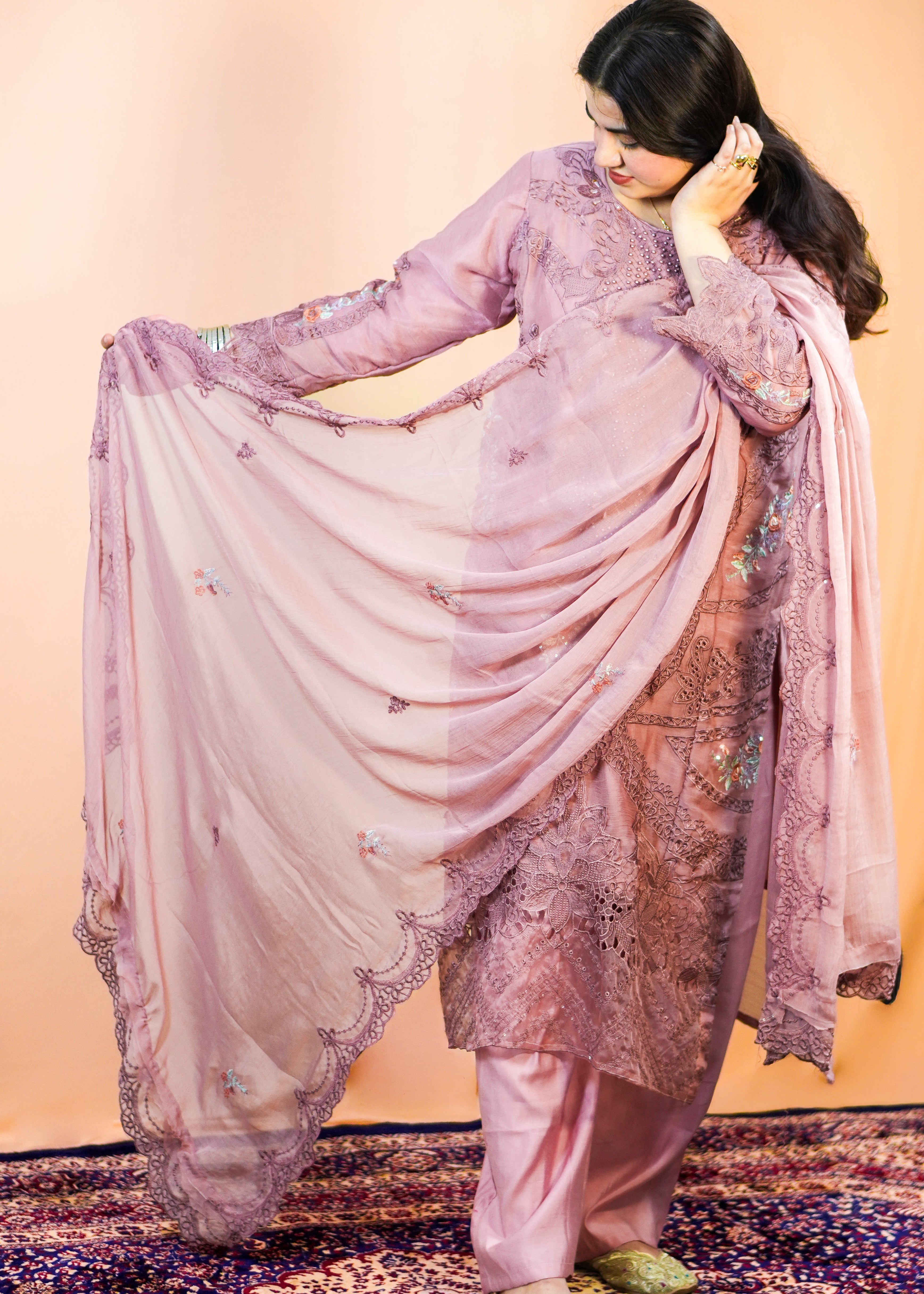 Woman in a pink traditional outfit with a floral pattern on a patterned rug.