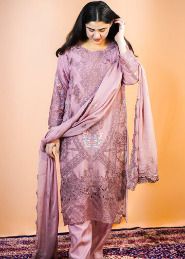 Woman in a traditional outfit with a pinkish-purple dupatta on a patterned rug.