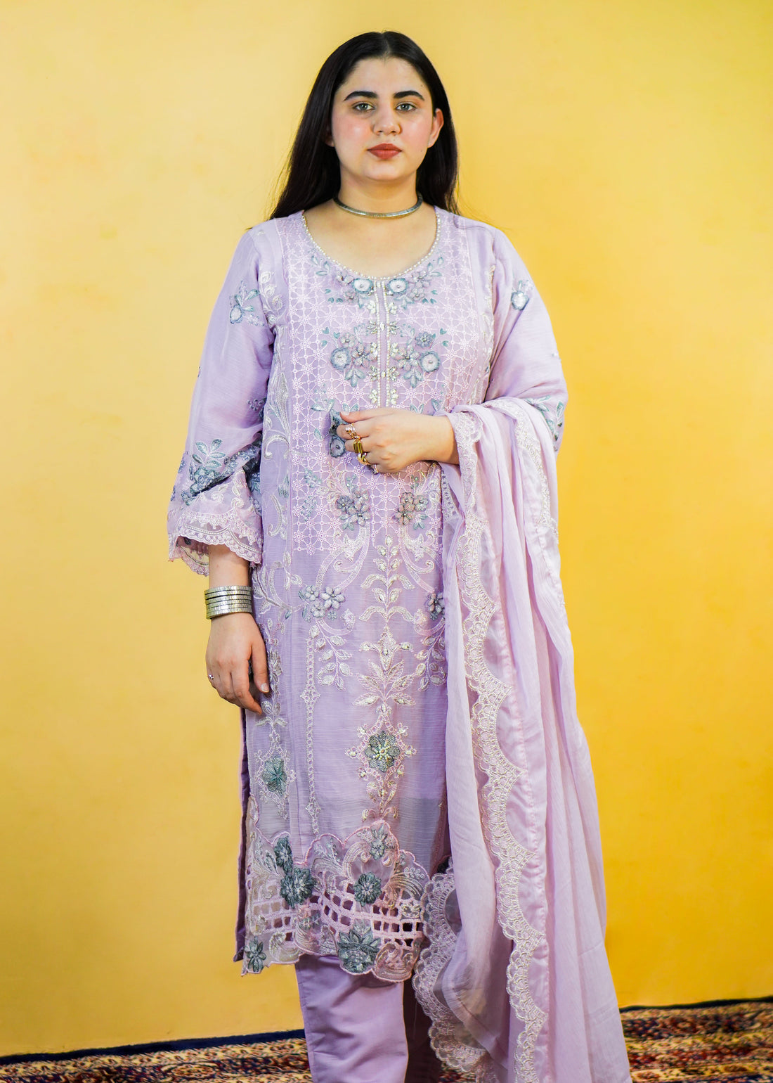 Woman wearing a light purple embroidered outfit with a matching dupatta against a yellow background