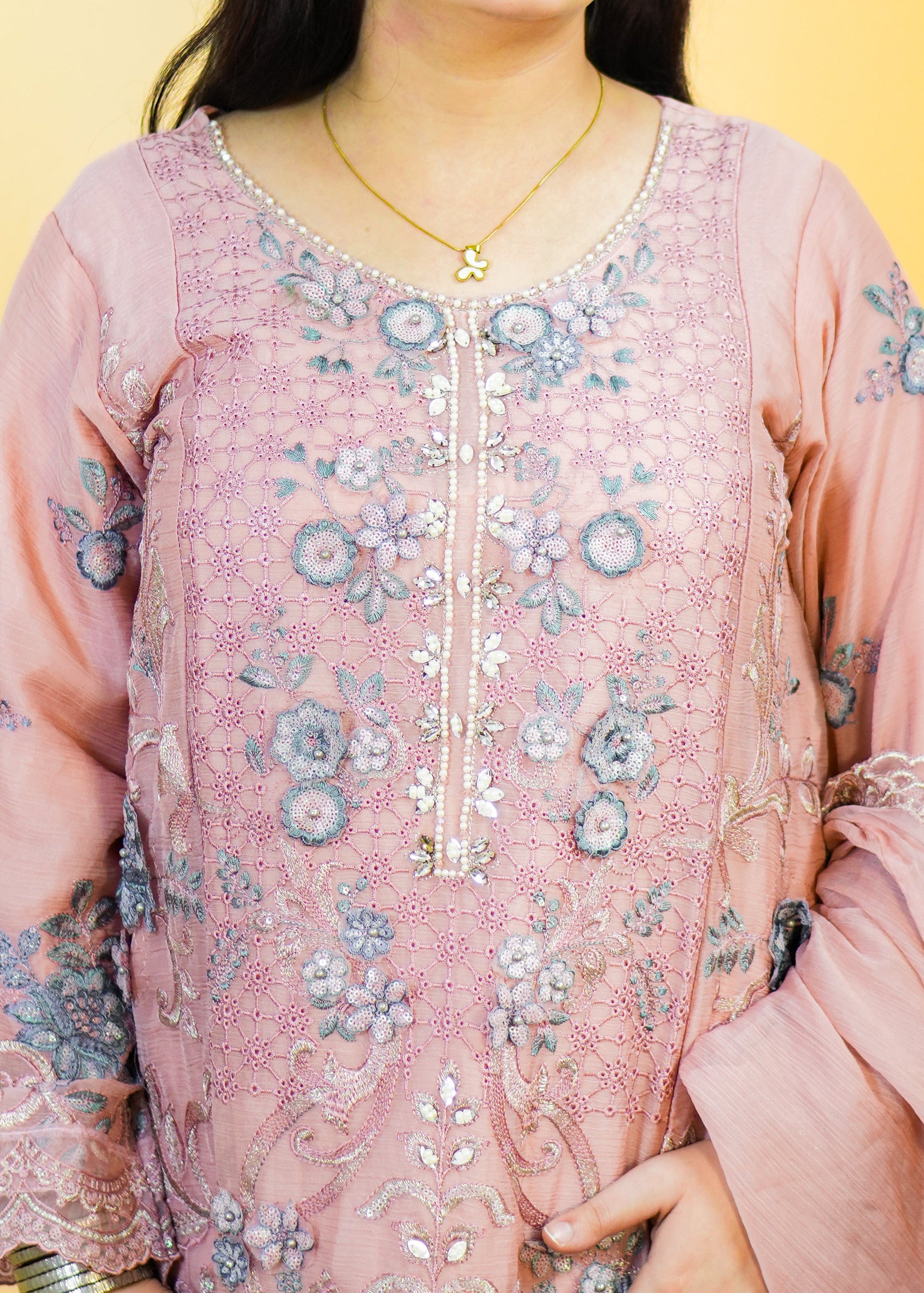 Woman wearing a pink embroidered traditional outfit against a yellow background