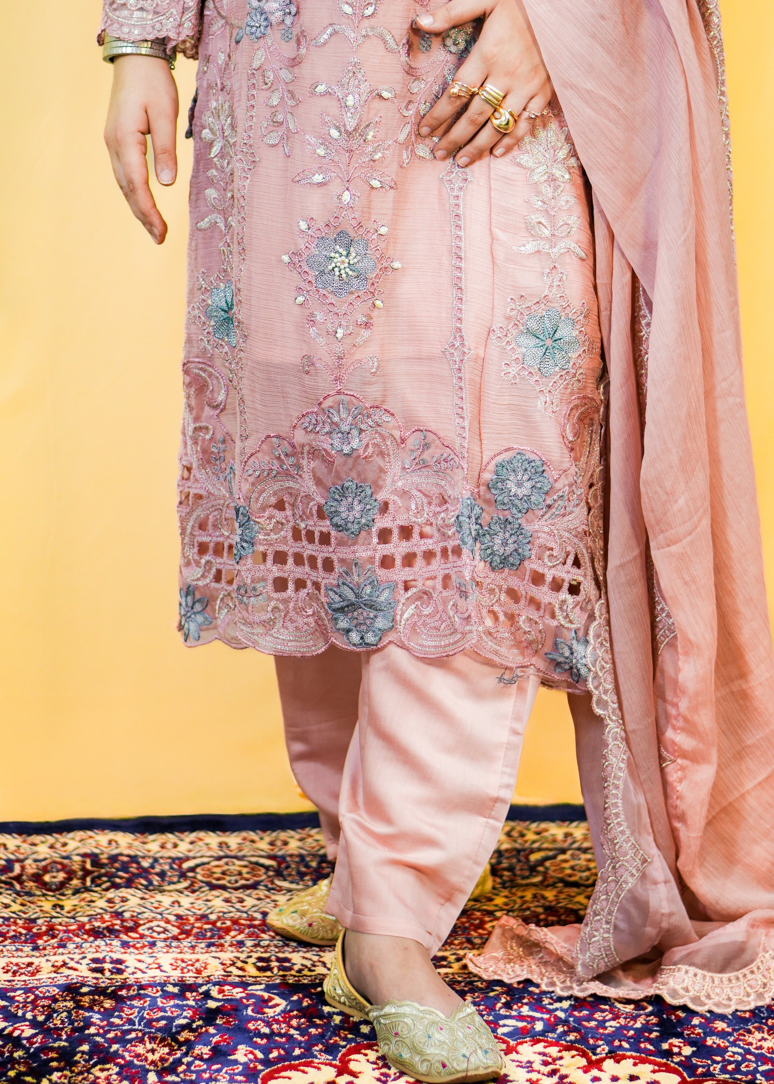 Person wearing a pink embroidered traditional outfit on a patterned rug with a yellow wall background