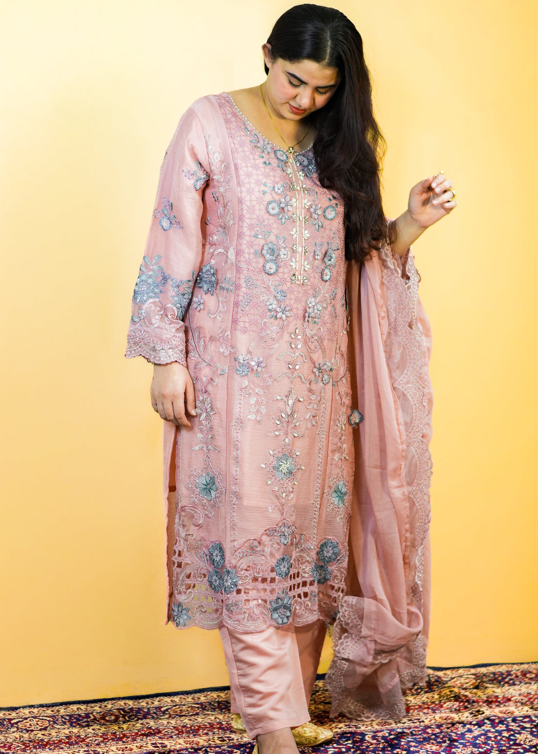 Woman in a pink traditional outfit standing on a patterned rug with a yellow background
