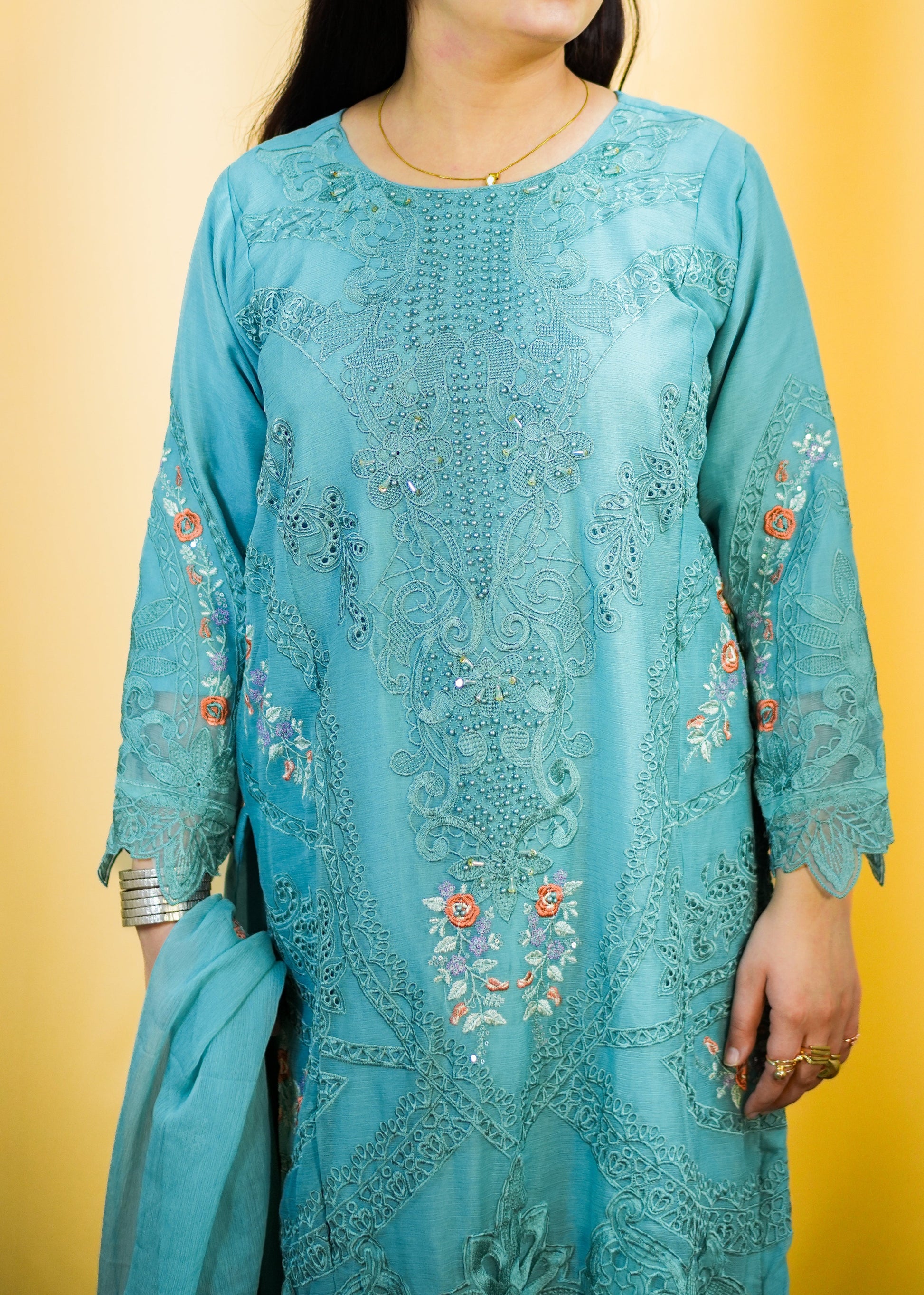 Woman wearing a light blue embroidered traditional outfit against a yellow background