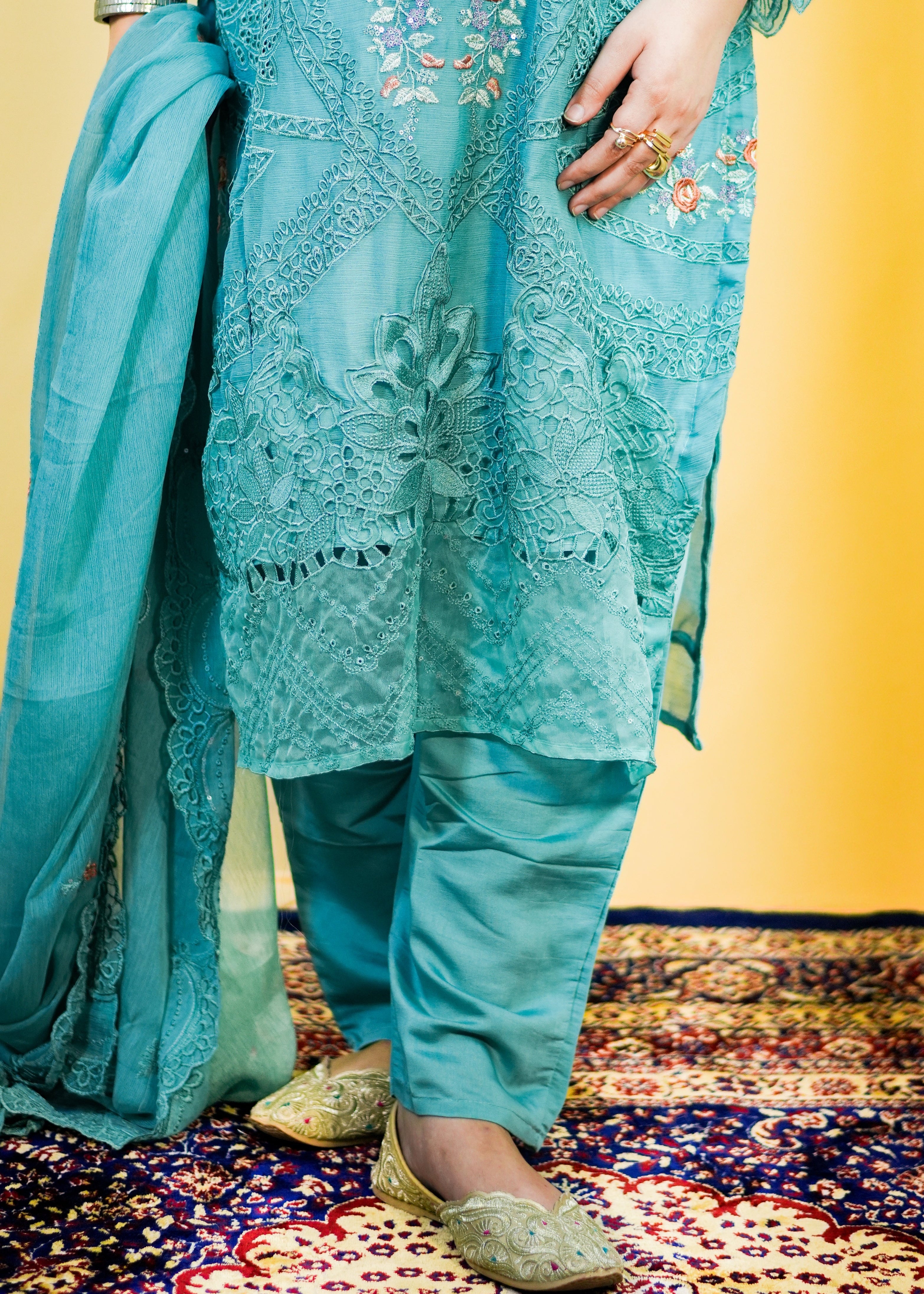 Person wearing a blue embroidered outfit on a patterned rug with a yellow wall background