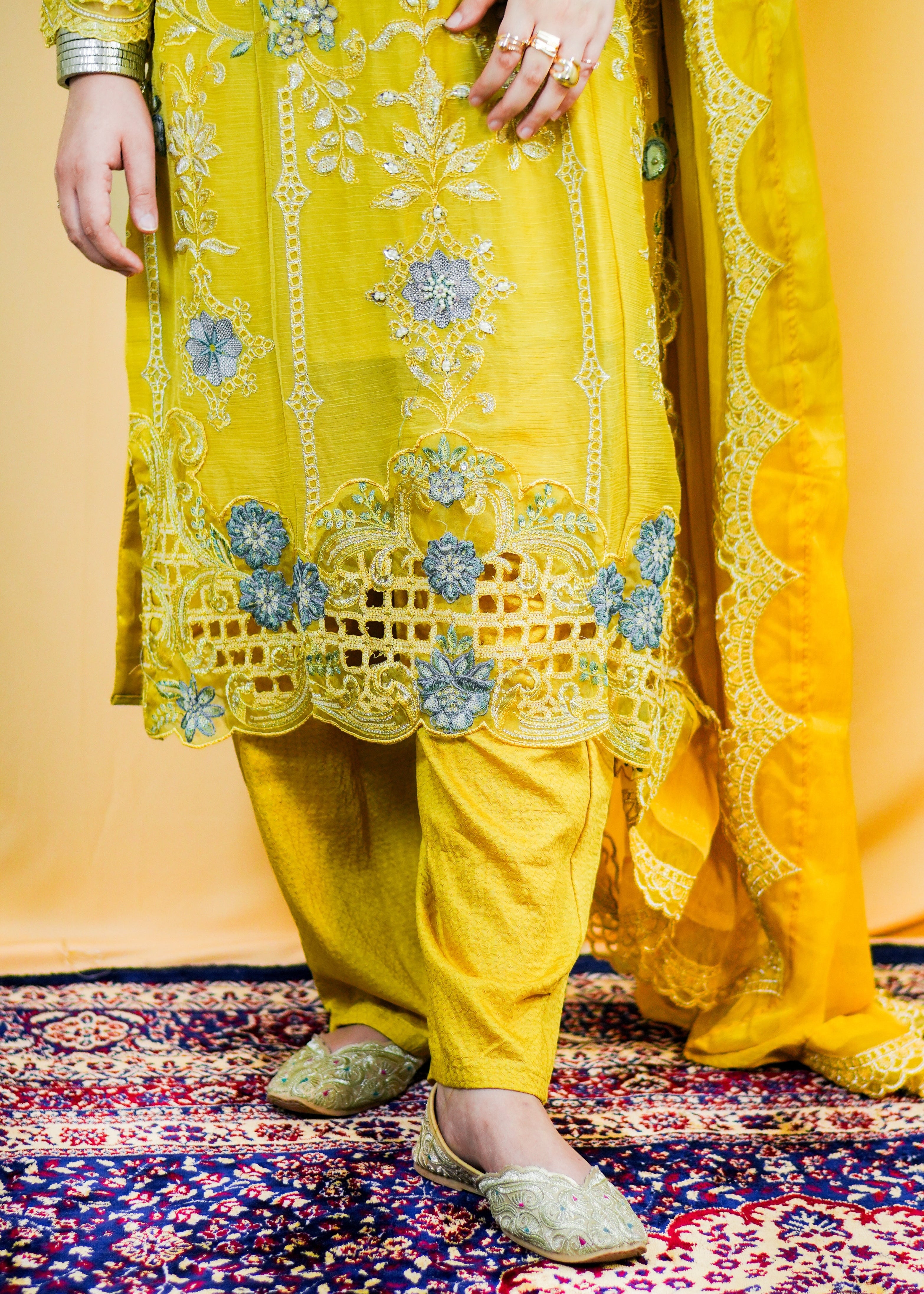 Person wearing a yellow embroidered outfit on a patterned rug.
