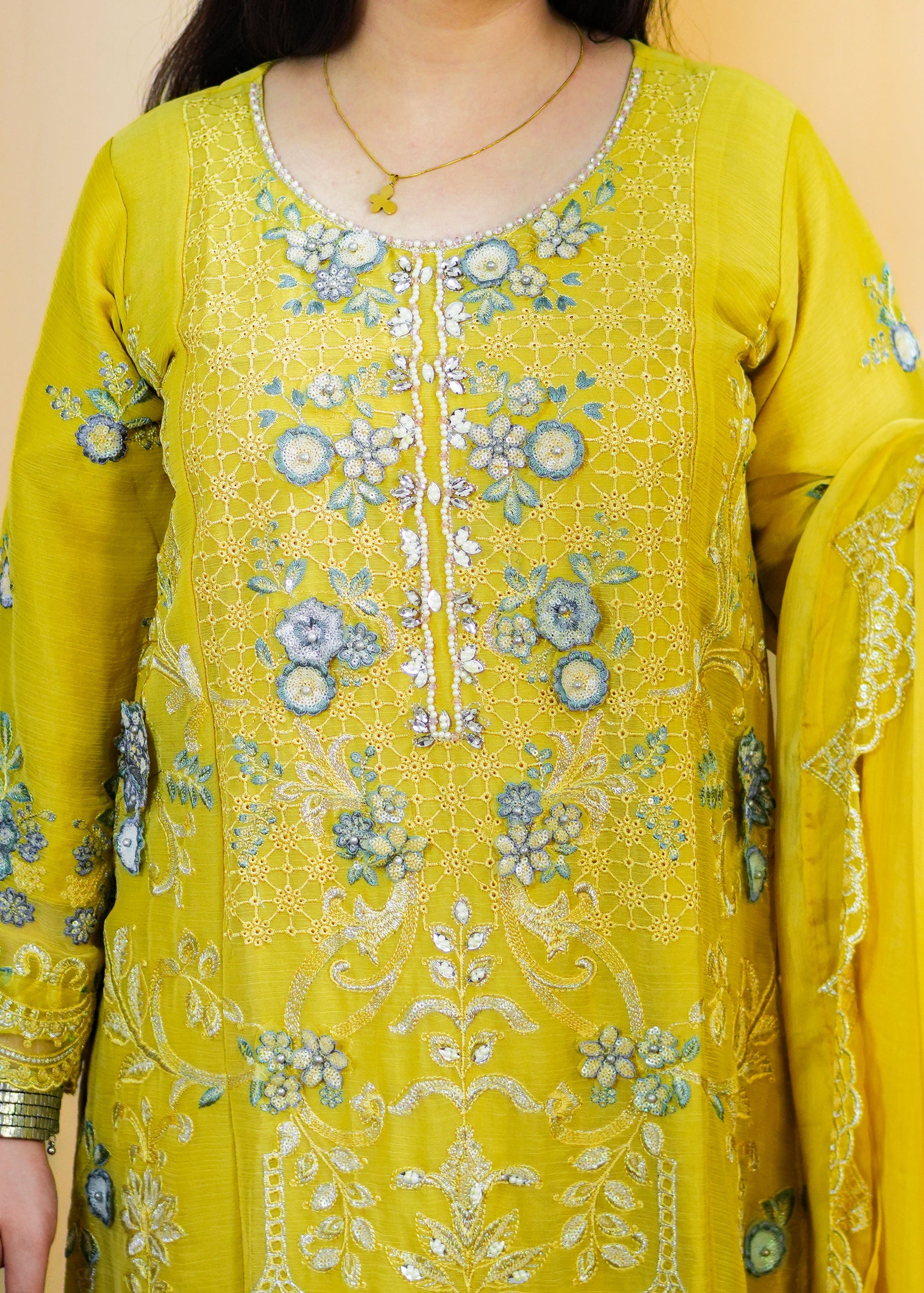 Woman wearing a yellow embroidered traditional outfit against a beige background