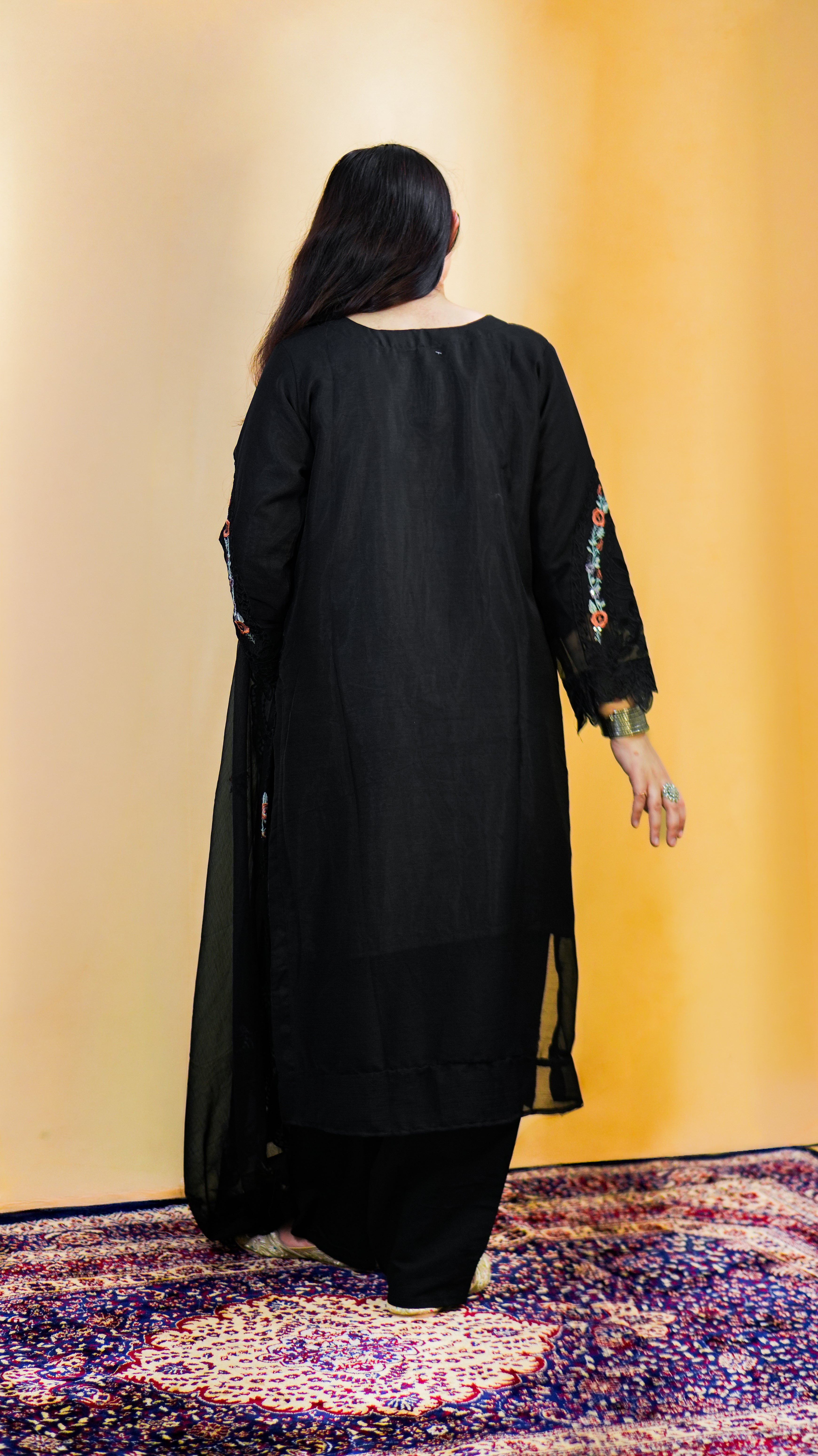 Person wearing a black outfit with floral sleeves on a patterned rug.