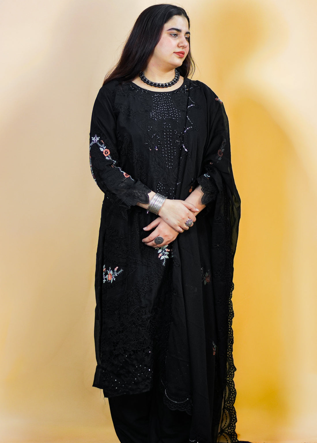 Woman wearing a black traditional outfit with floral embroidery against a warm-toned background