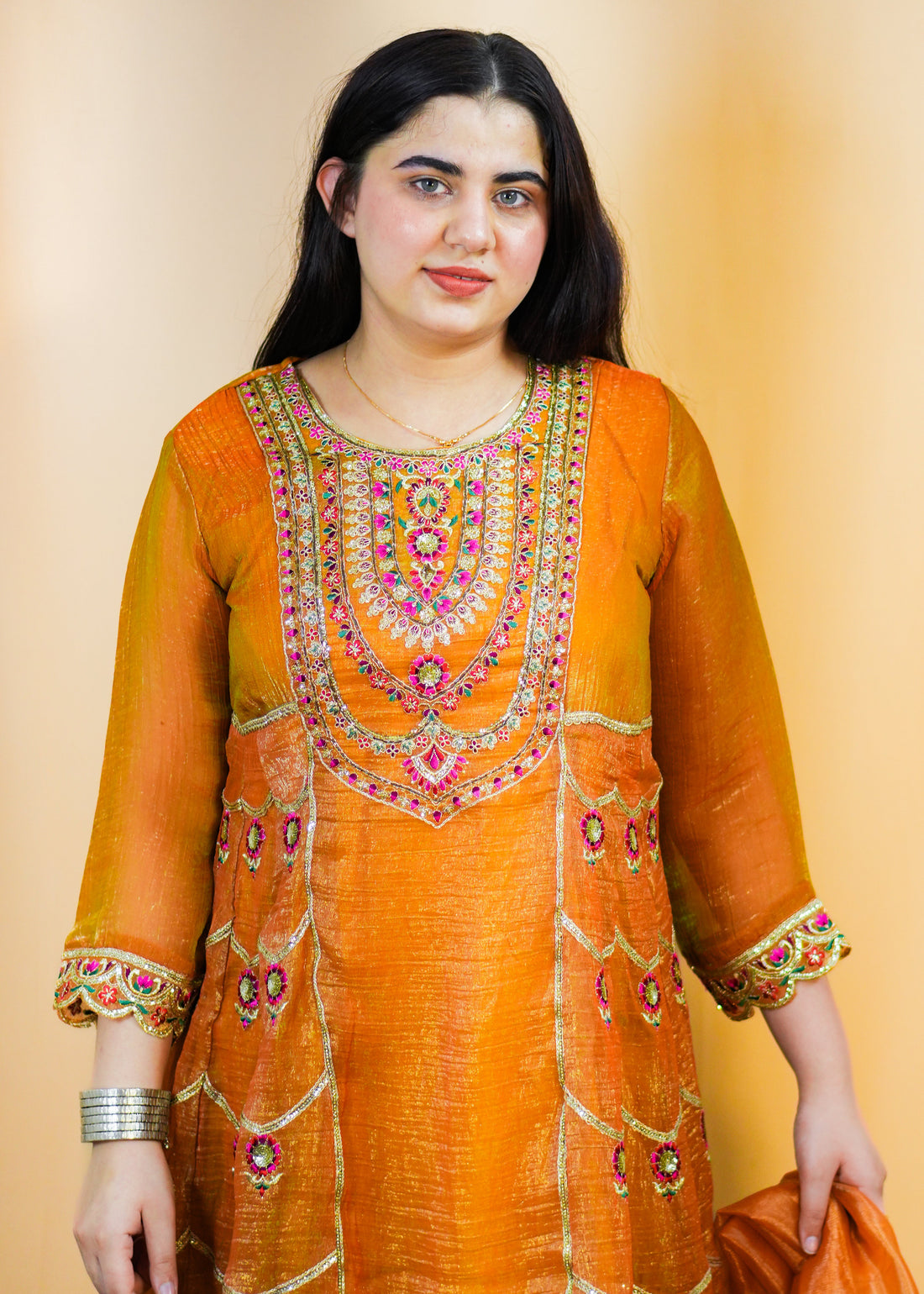 Woman in an orange traditional outfit with a matching dupatta on a patterned rug.