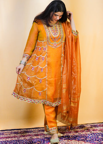 Woman in an orange traditional outfit with a matching dupatta on a patterned rug.