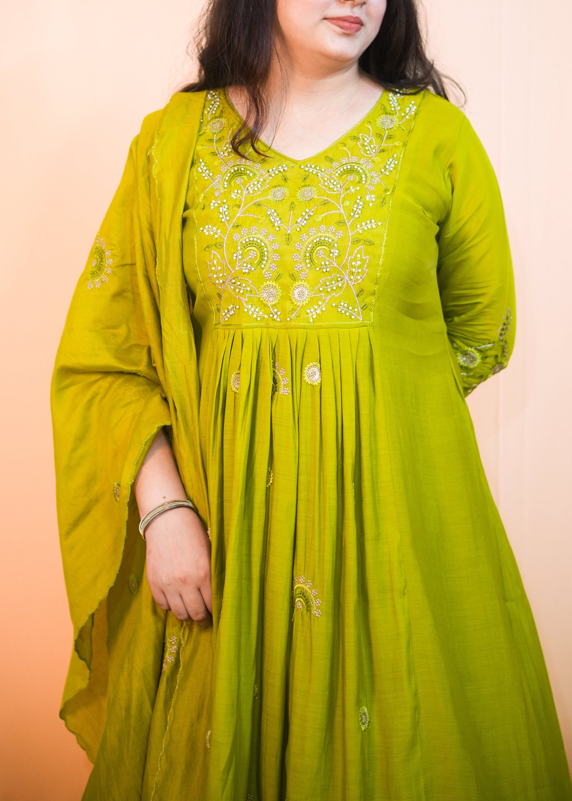 Woman wearing a green embroidered dress against a pink background