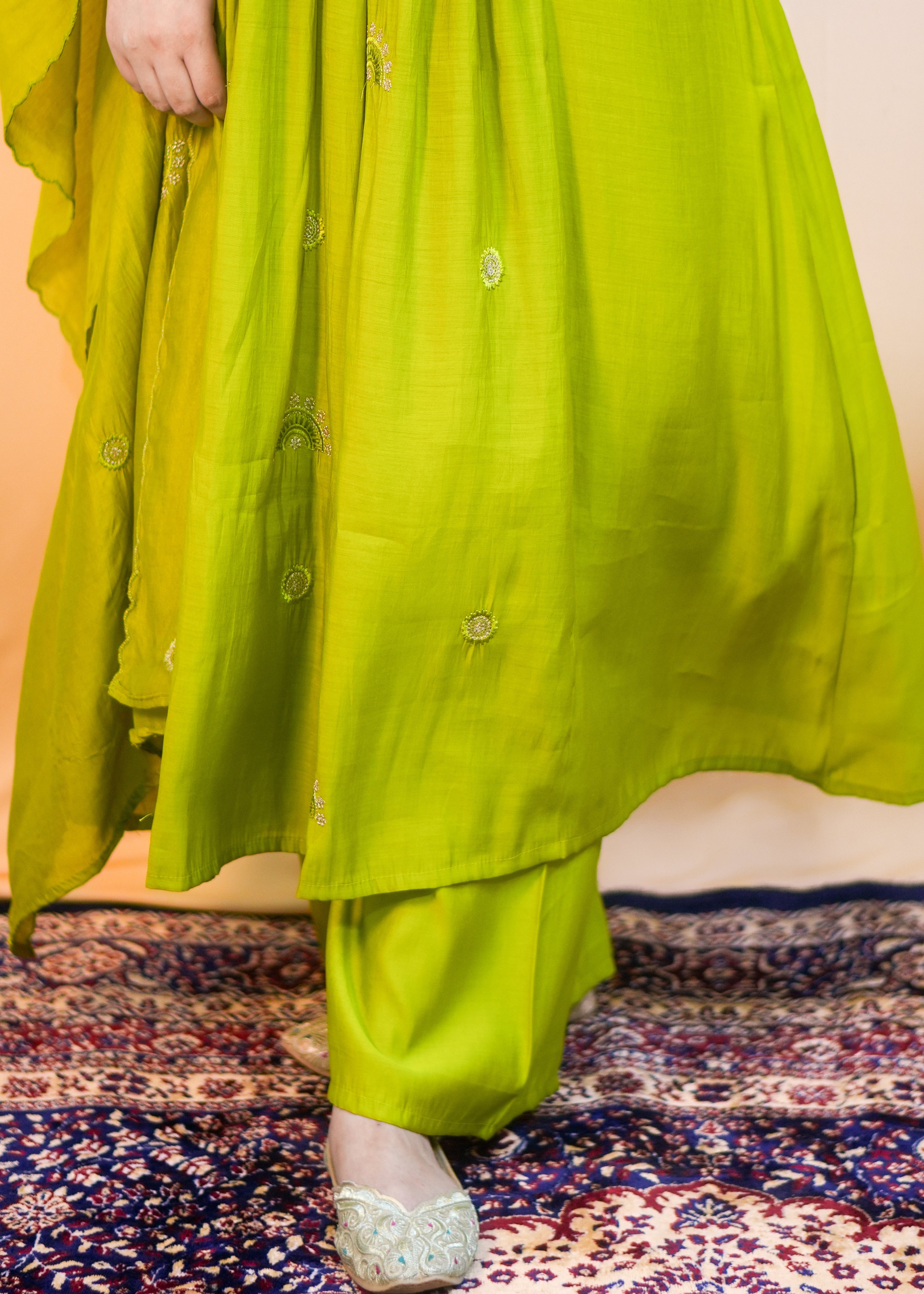 Person wearing a bright green traditional outfit on a patterned rug