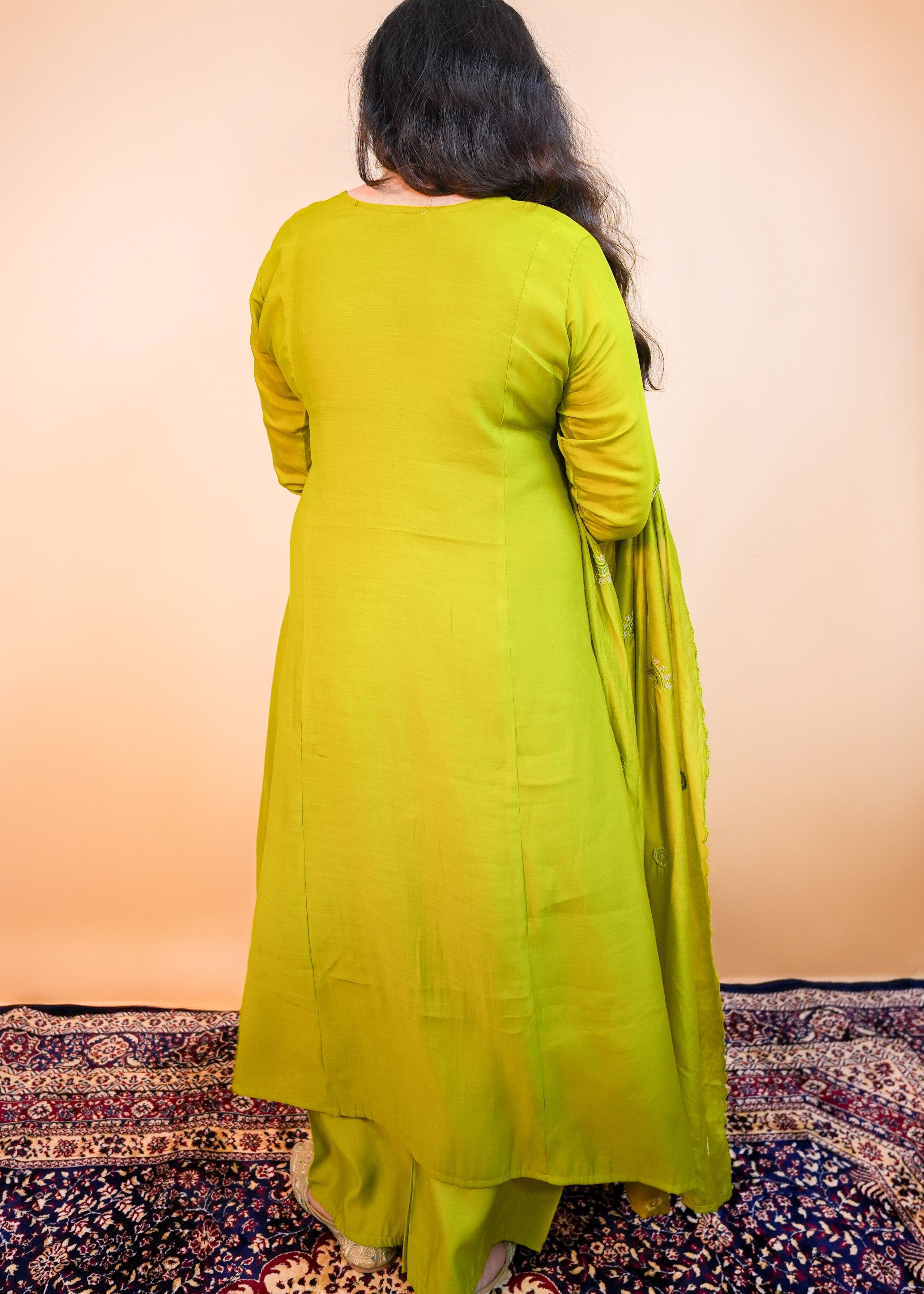 Person wearing a bright green dress standing on a patterned rug with an orange wall background