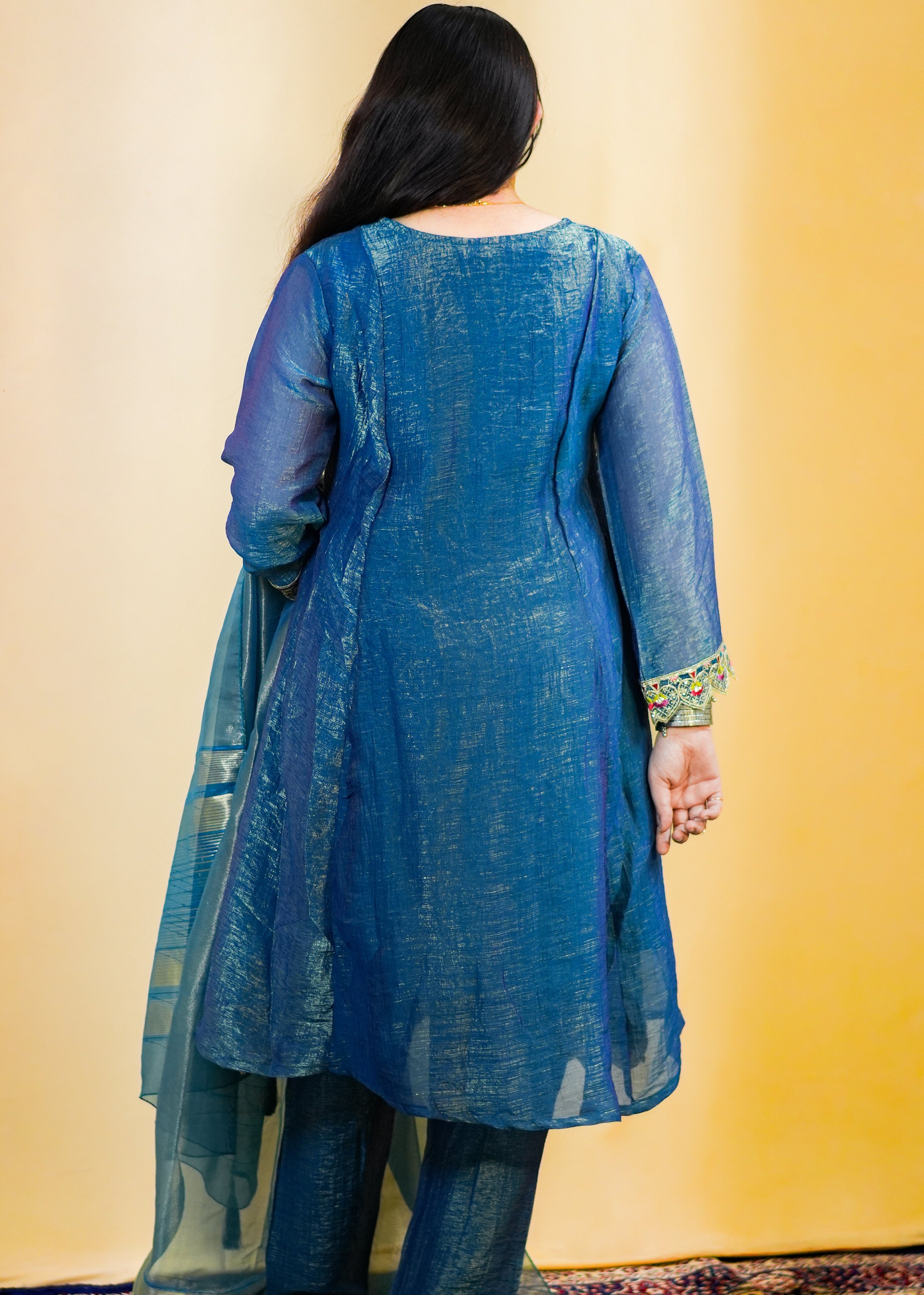 Woman wearing a blue traditional outfit against a yellow wall.