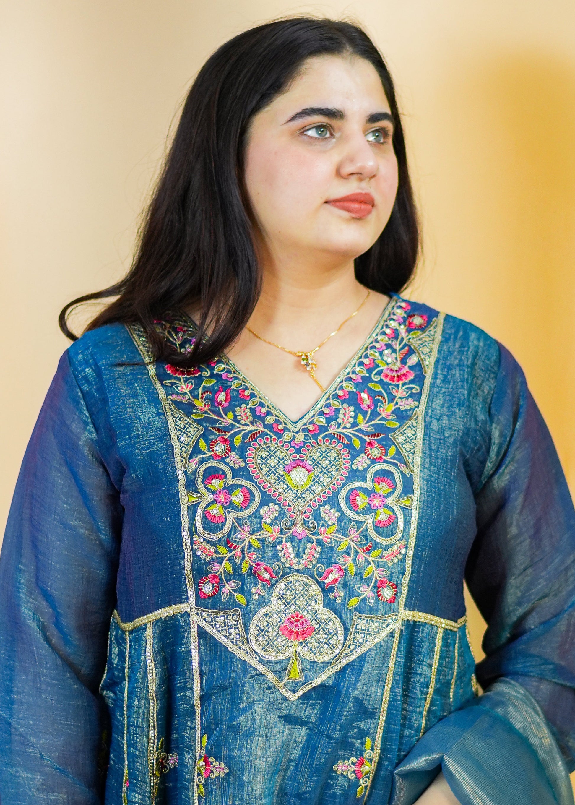 Woman wearing a blue embroidered traditional outfit against a beige background