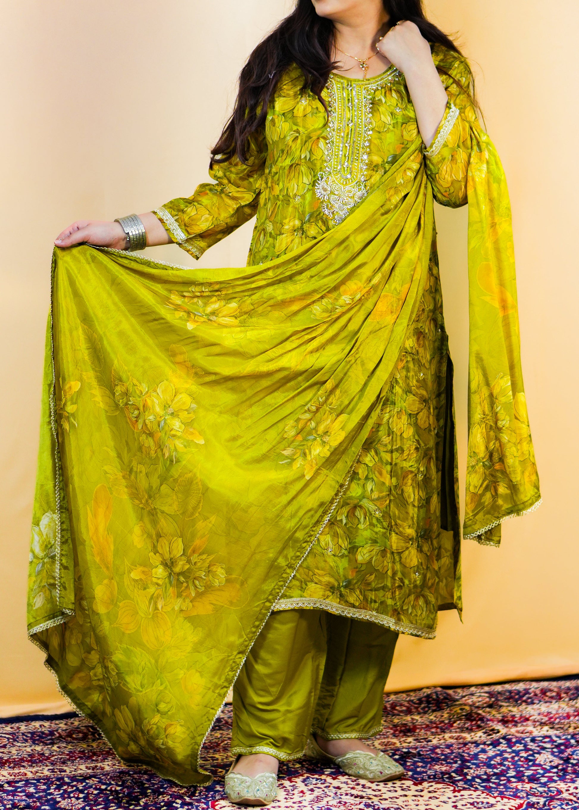 Woman in a green traditional outfit standing on a patterned rug with a yellow background