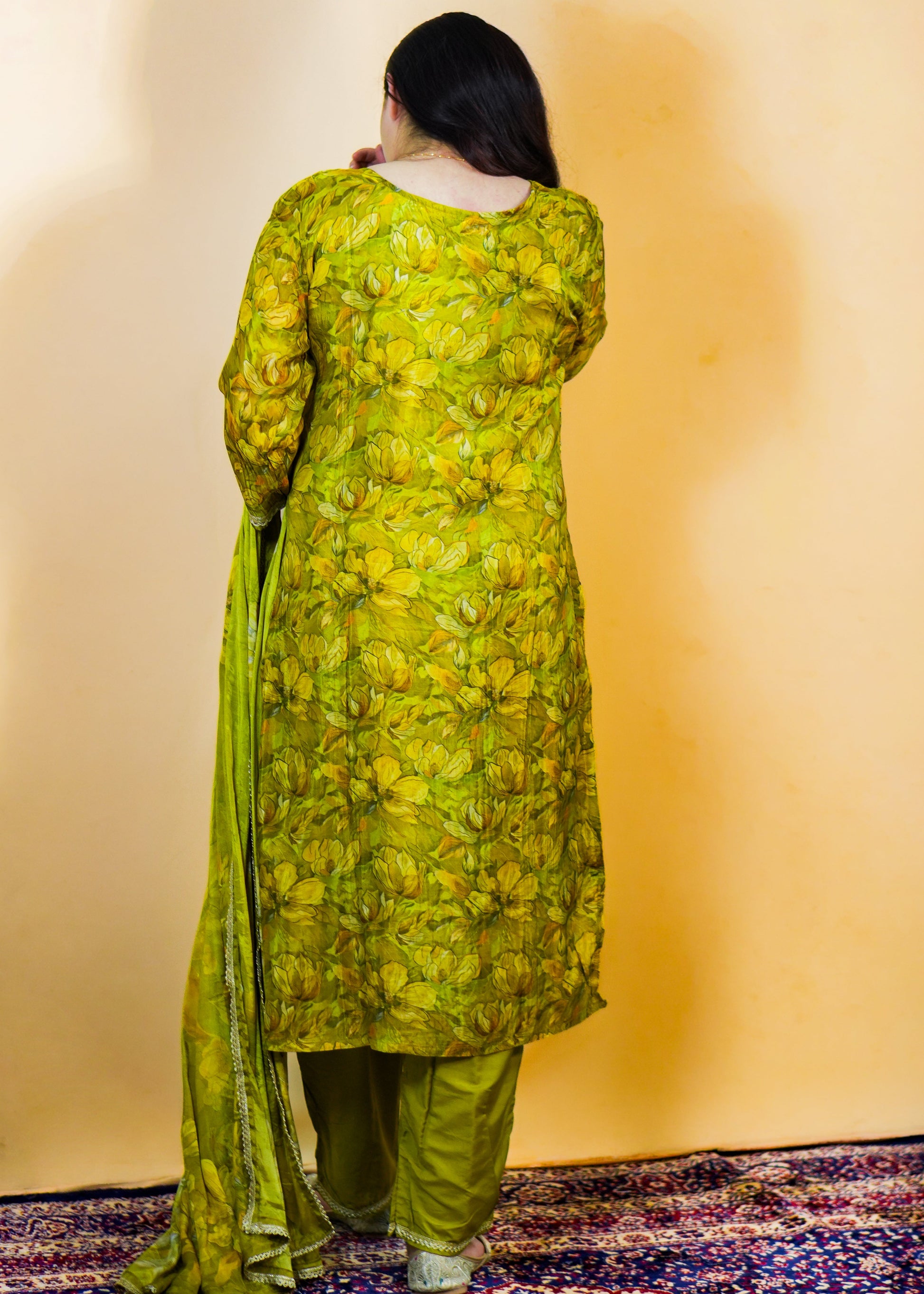 Person wearing a green floral kurta with pants against a plain wall.
