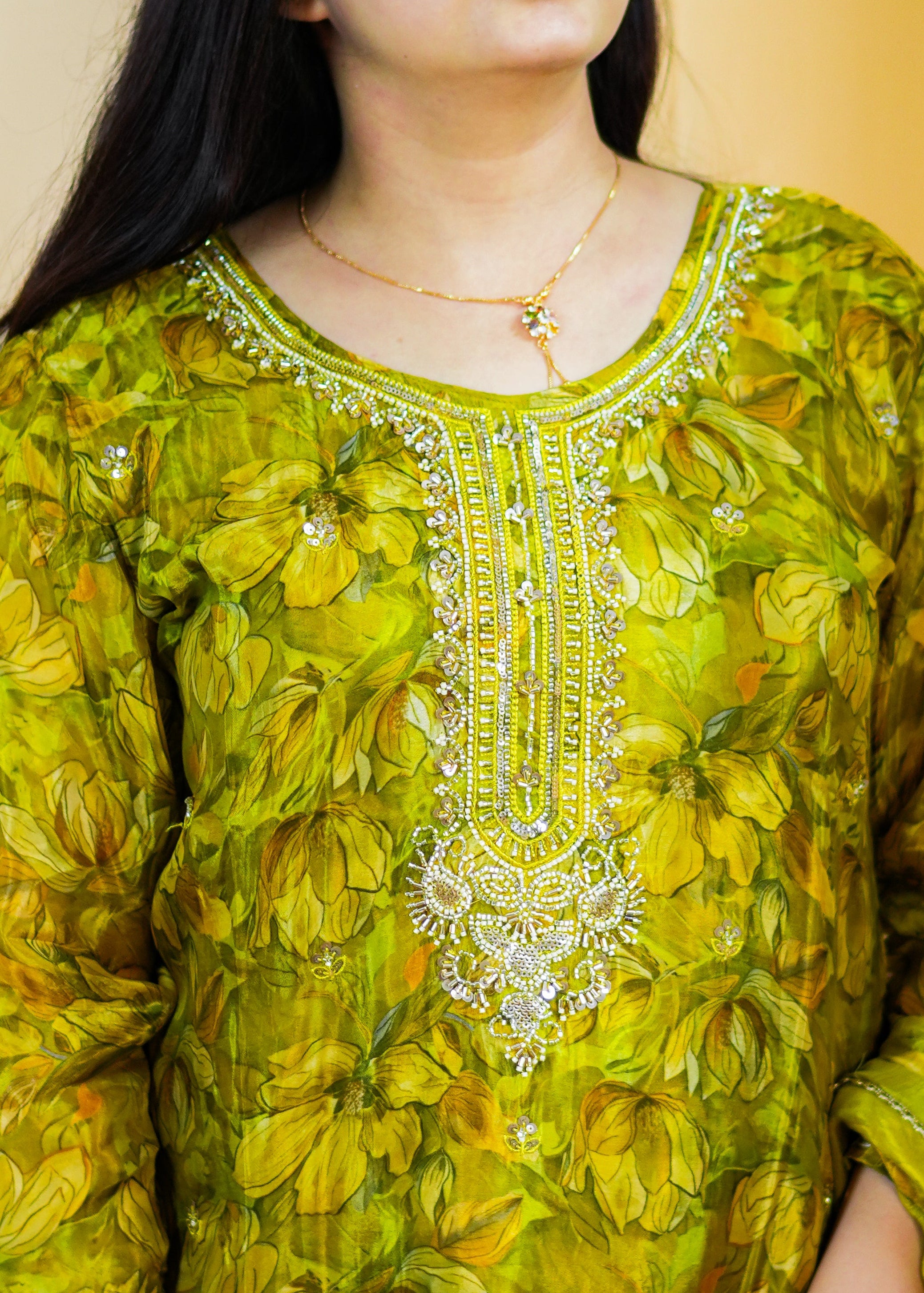 Woman wearing a green traditional outfit with intricate patterns against a beige background