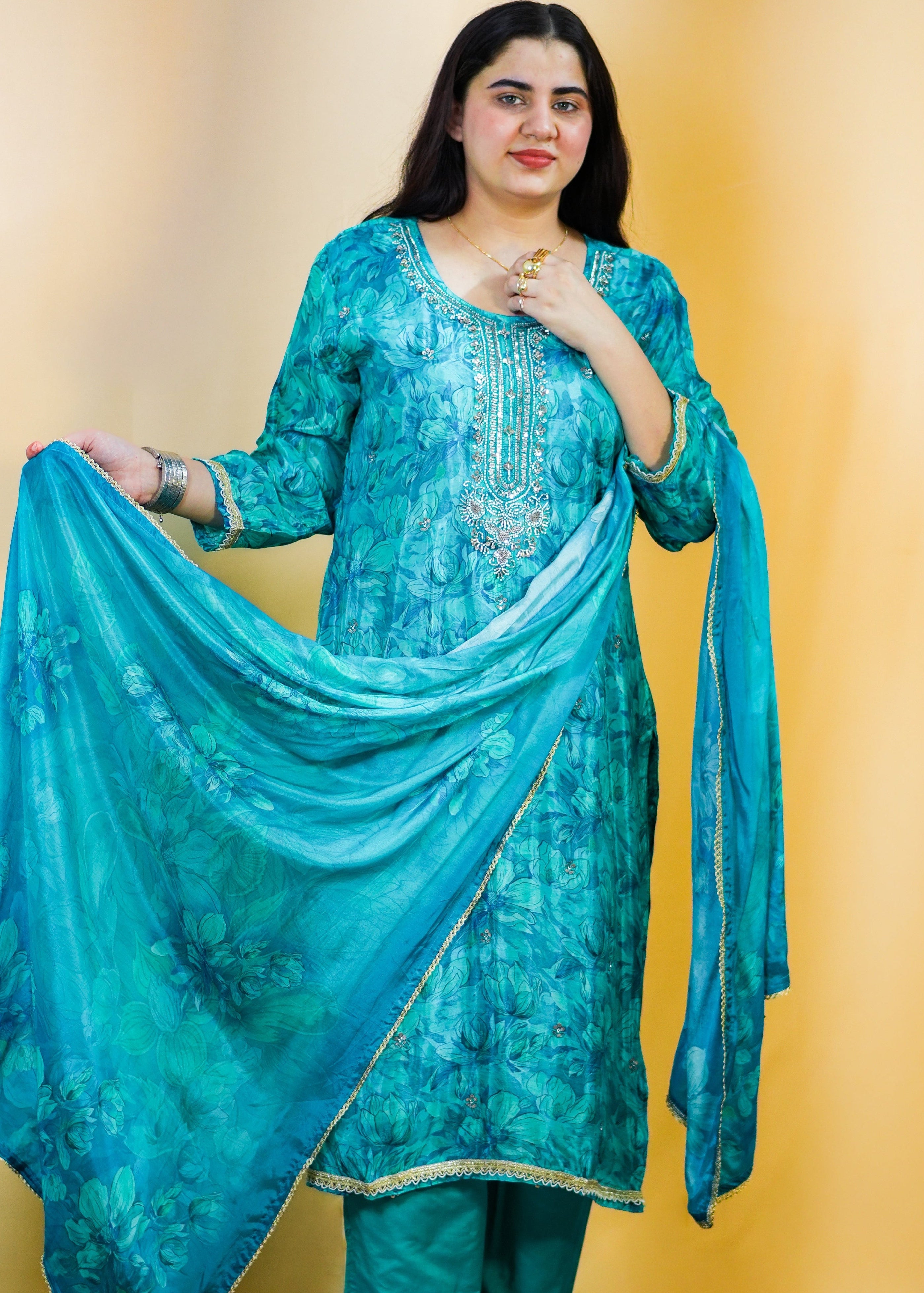 Woman in a blue traditional outfit standing on a patterned rug with a yellow wall background