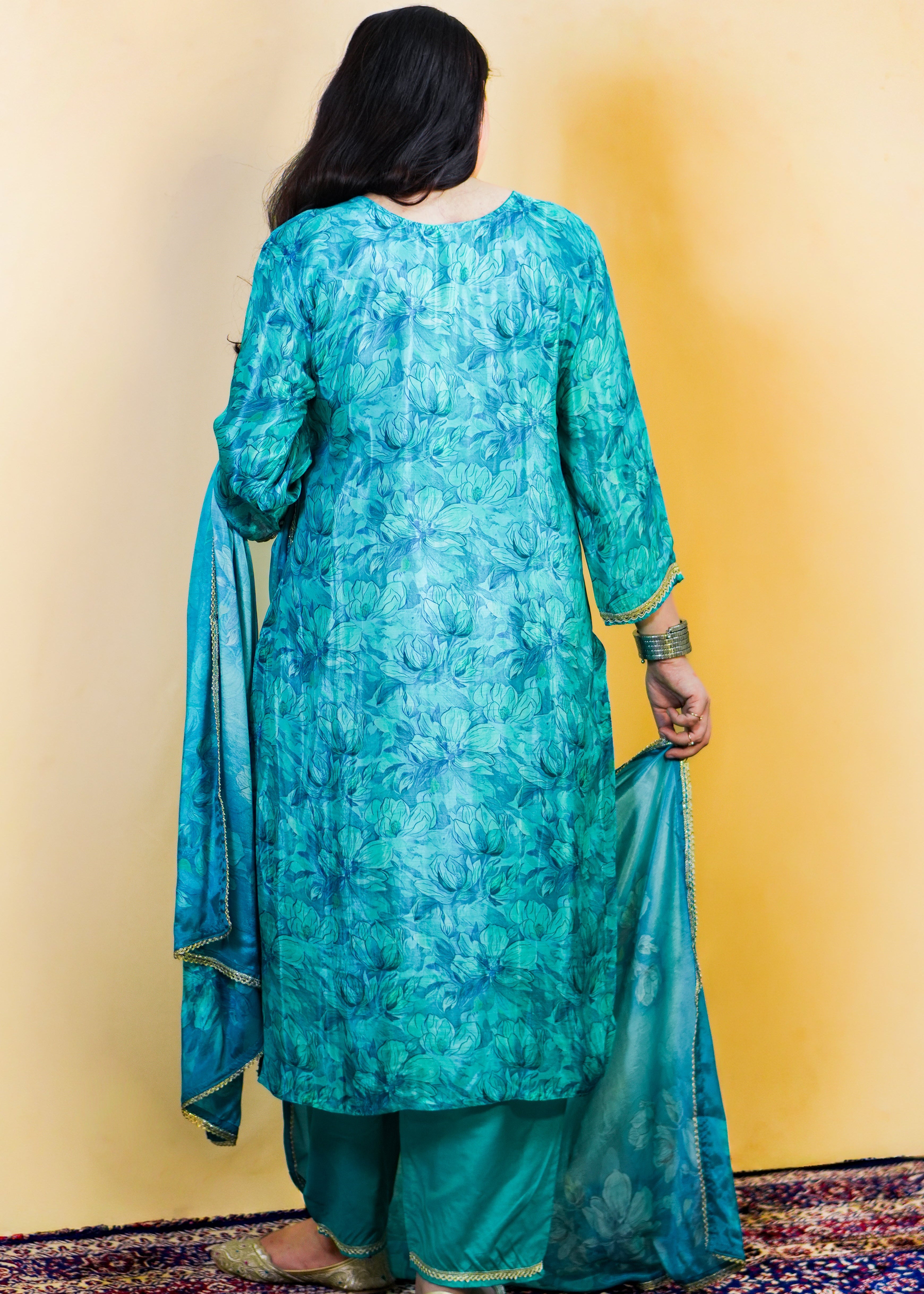 Person wearing a teal kurta with a matching dupatta against a yellow wall.