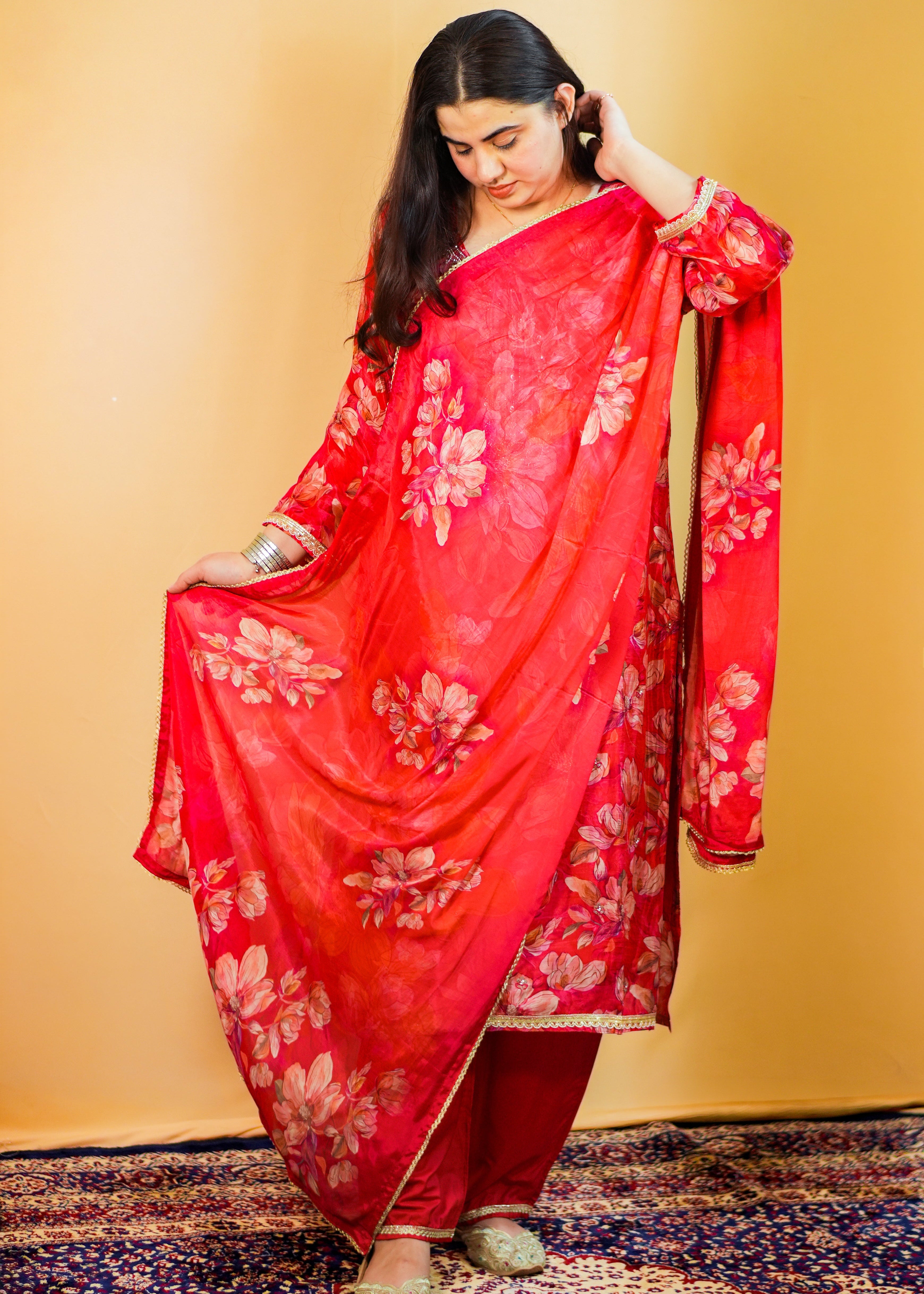 Woman in a red floral traditional outfit standing on a patterned rug with a yellow wall background