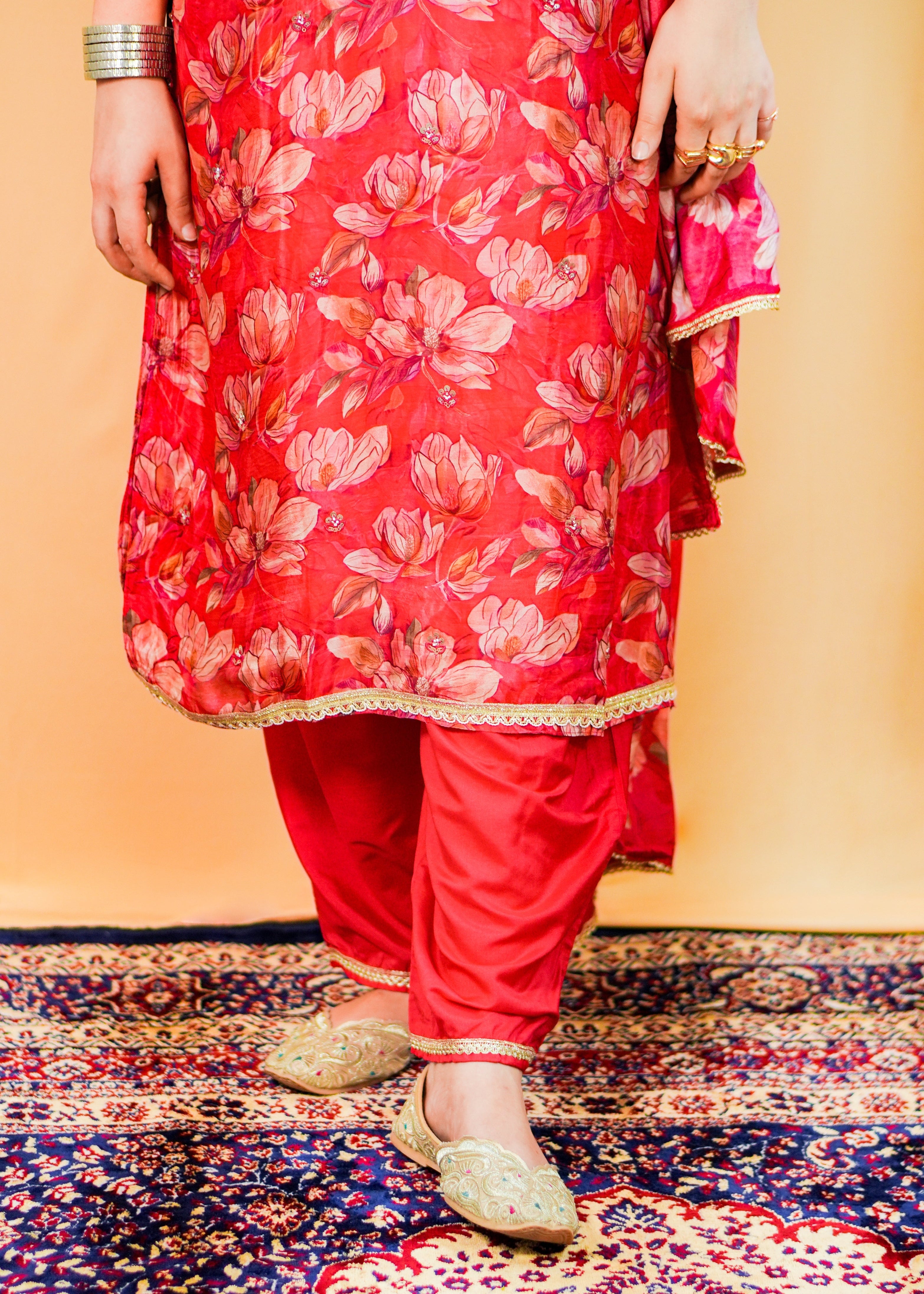 Person wearing a red floral traditional outfit standing on a patterned rug.