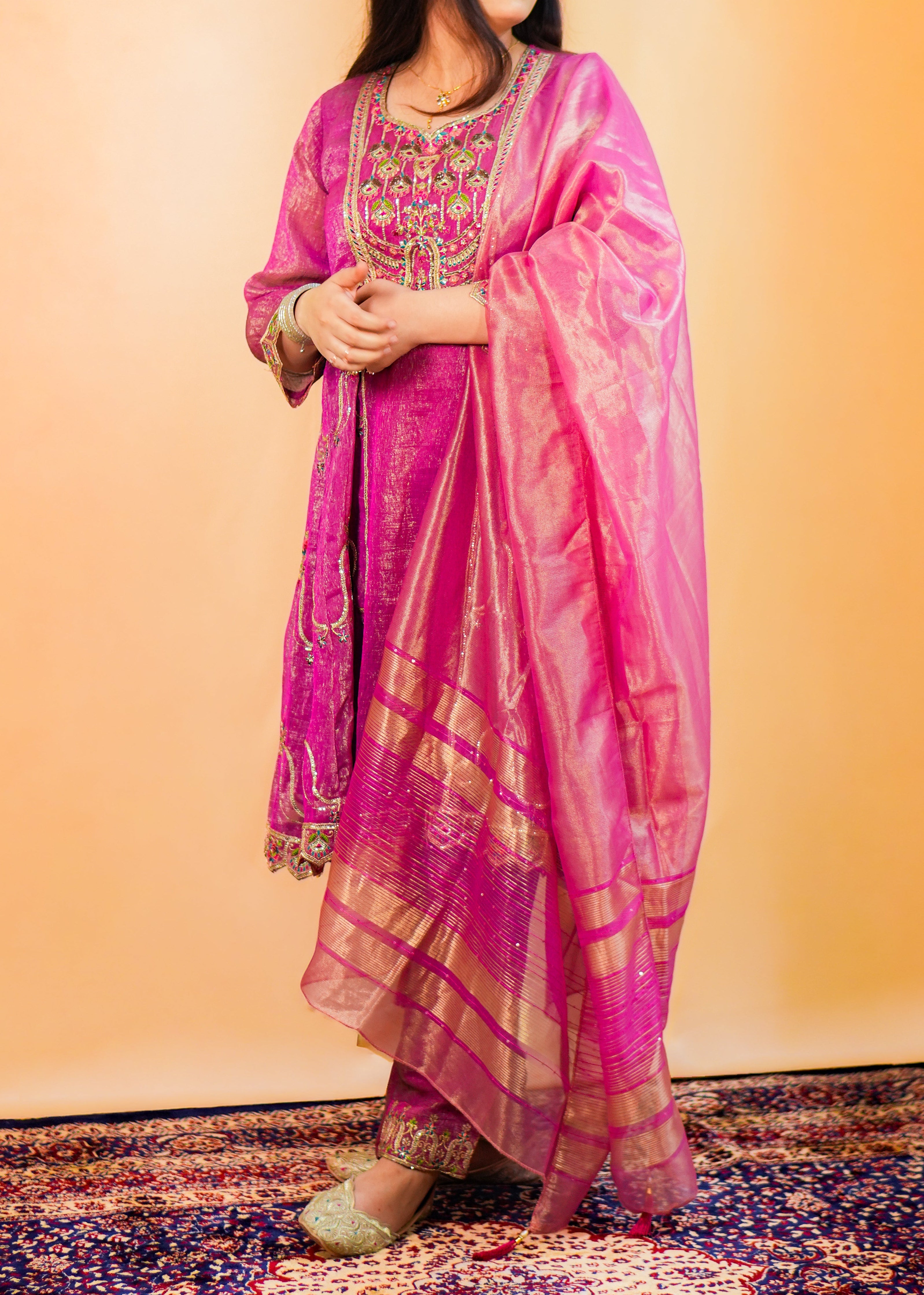 Woman in a pink traditional outfit standing on a patterned rug with a plain background