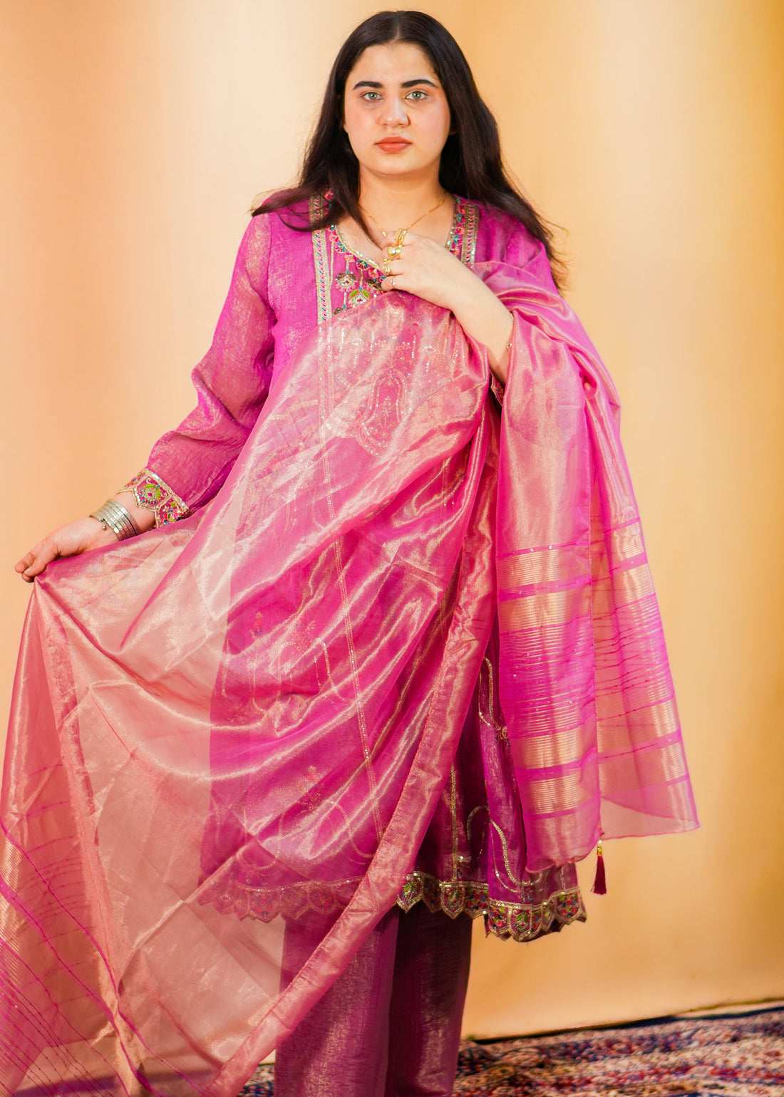 Woman in a pink dress with a gold border on a patterned rug.