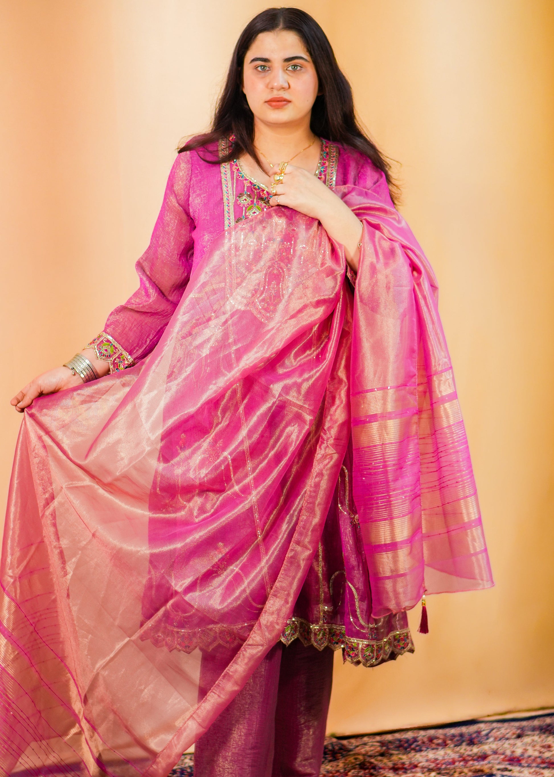 Woman in a pink dress with a gold border on a patterned rug.