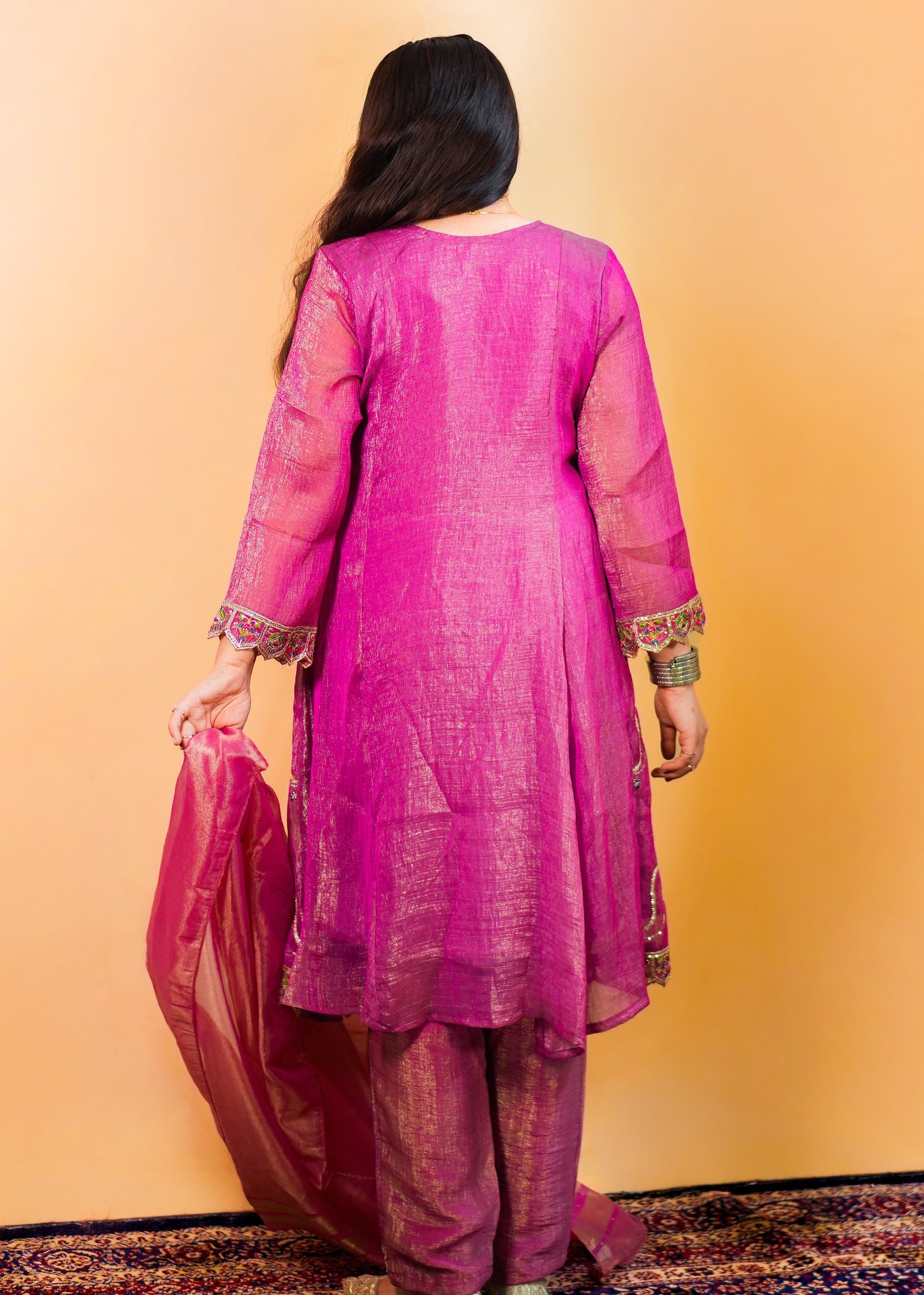 Person wearing a pink traditional outfit against an orange wall.