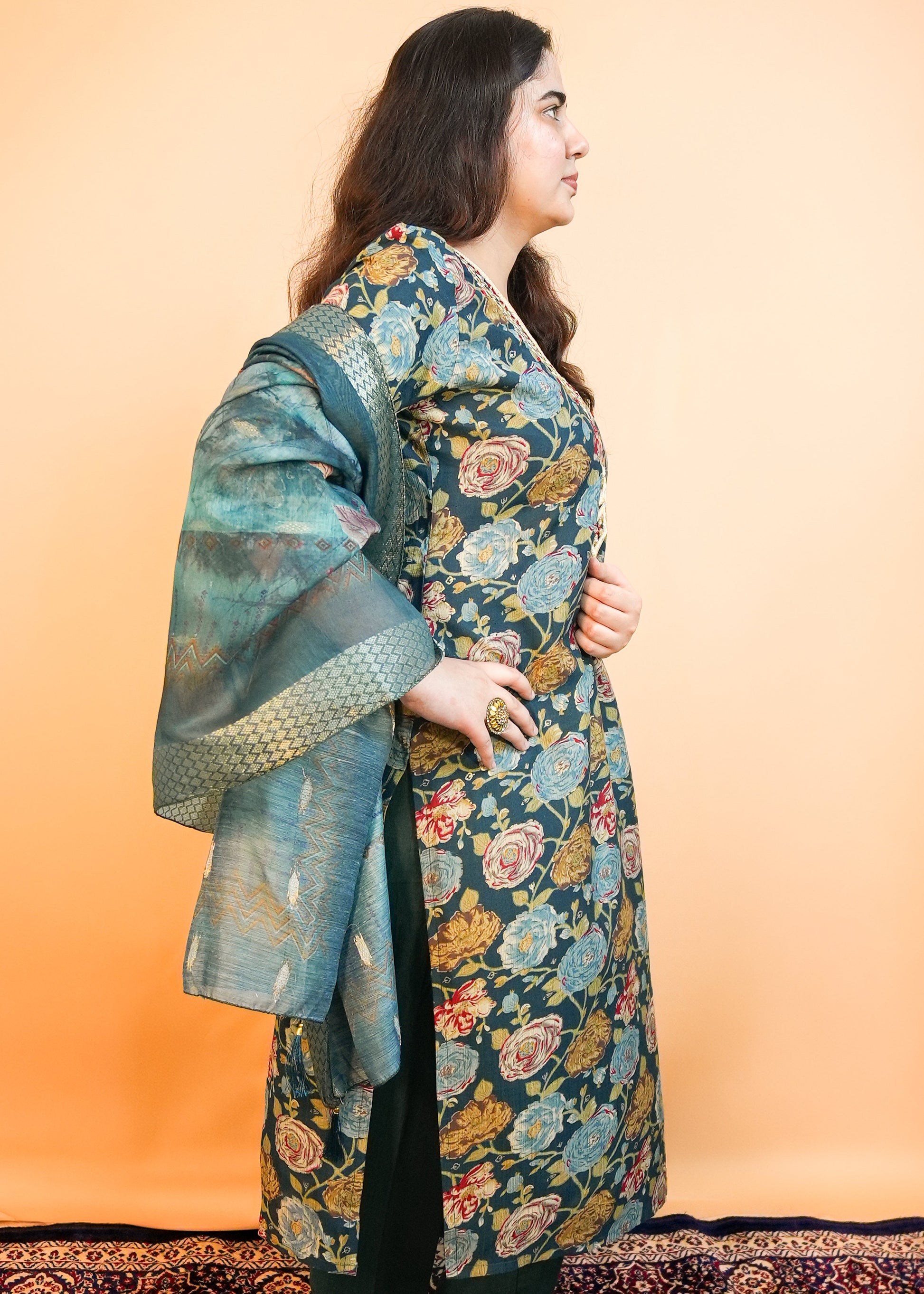 Woman wearing a floral patterned outfit standing against an orange wall.