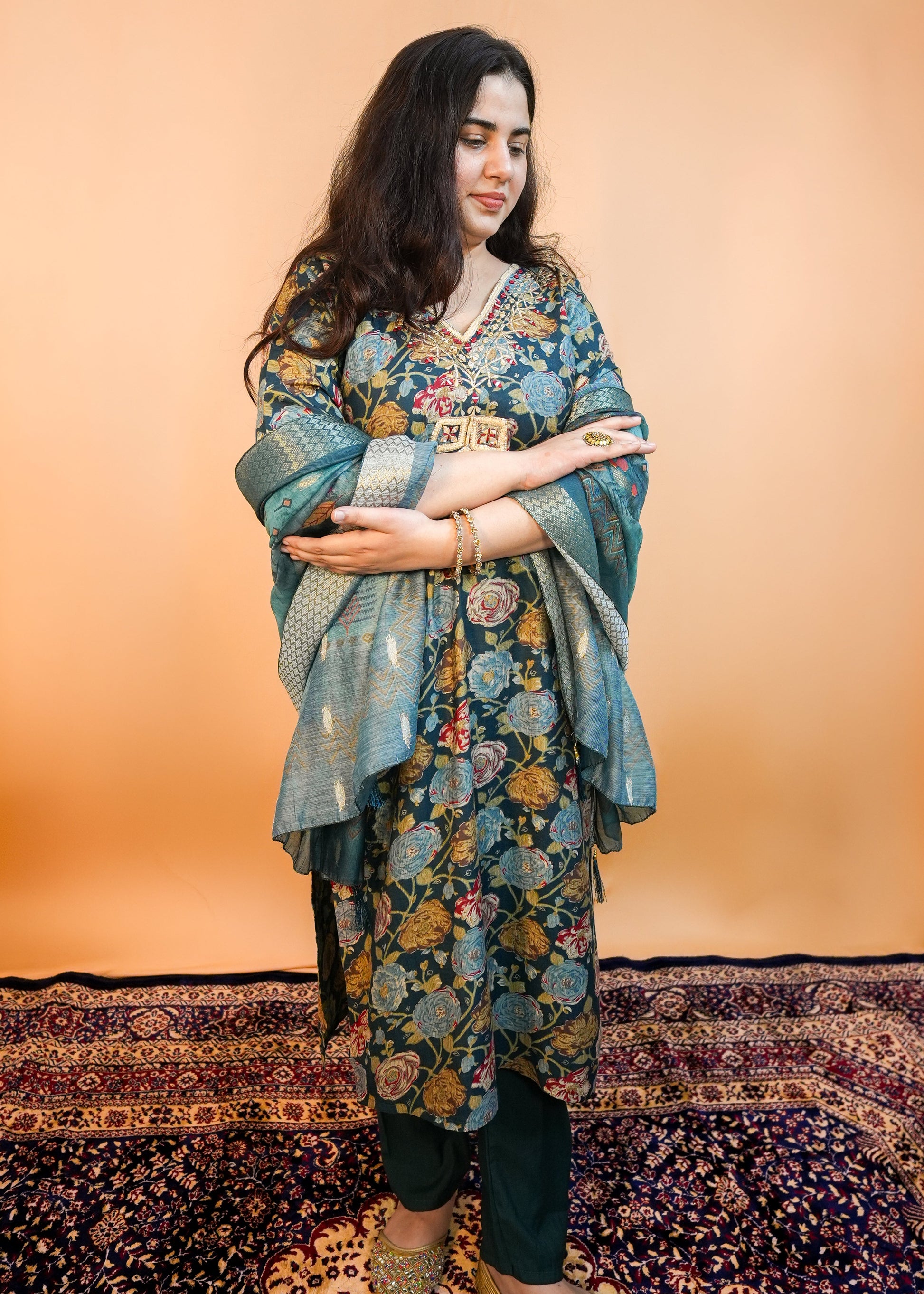 Woman wearing a floral dress with a patterned rug and wall in the background