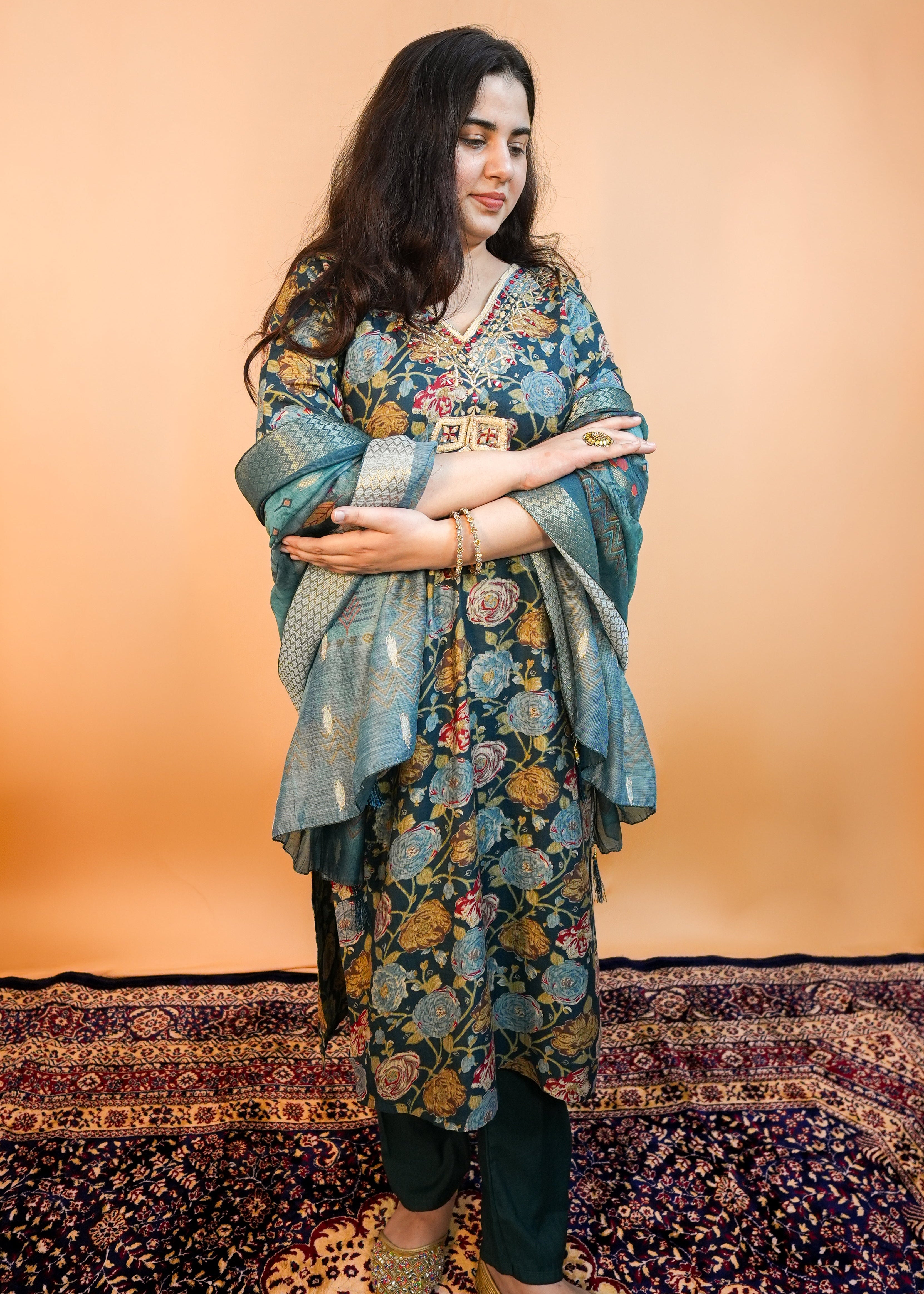 Woman wearing a floral dress with a patterned rug and wall in the background