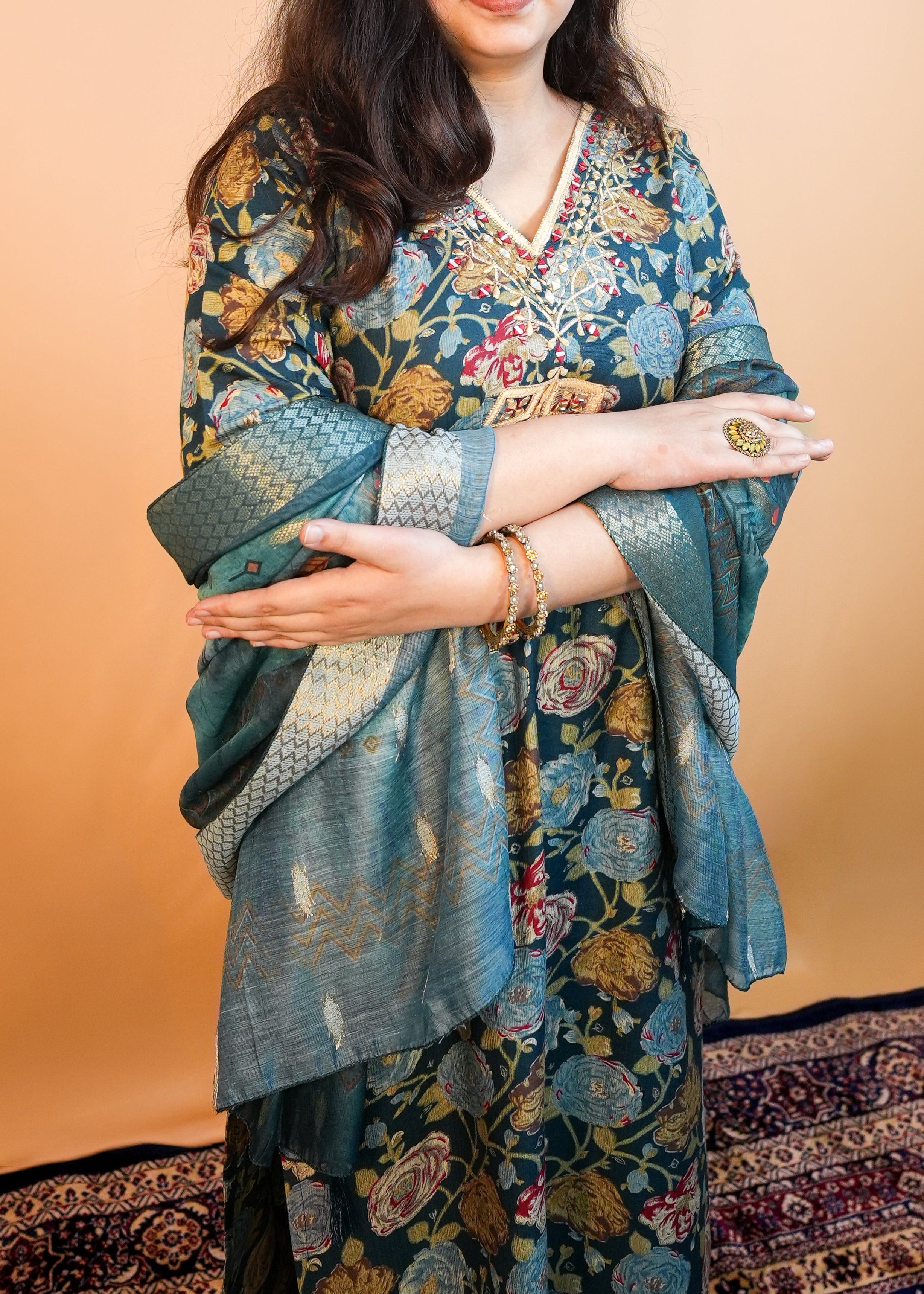 Woman wearing a floral traditional outfit against a beige wall.
