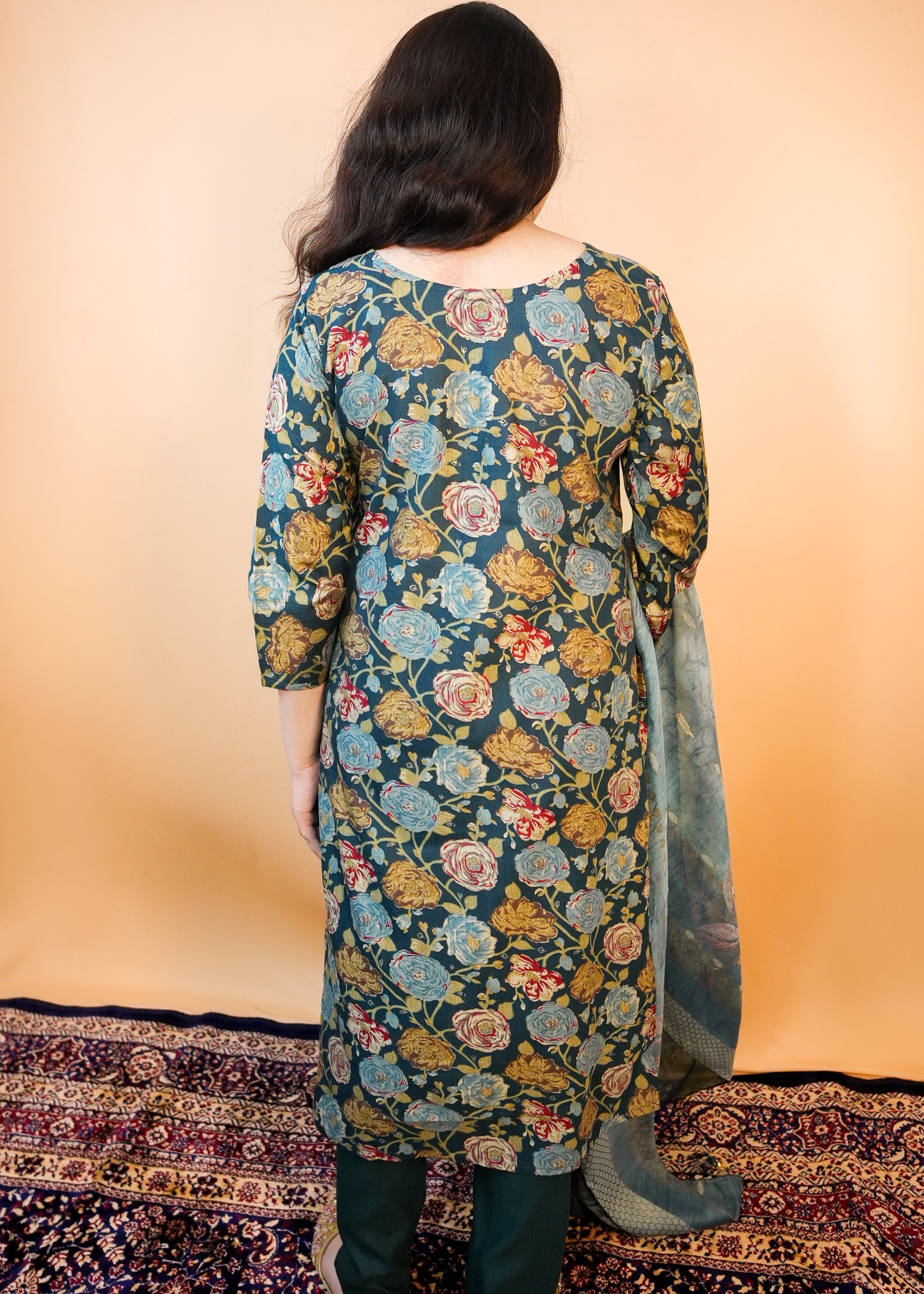 Person wearing a floral patterned kurta standing on a patterned rug with a plain background