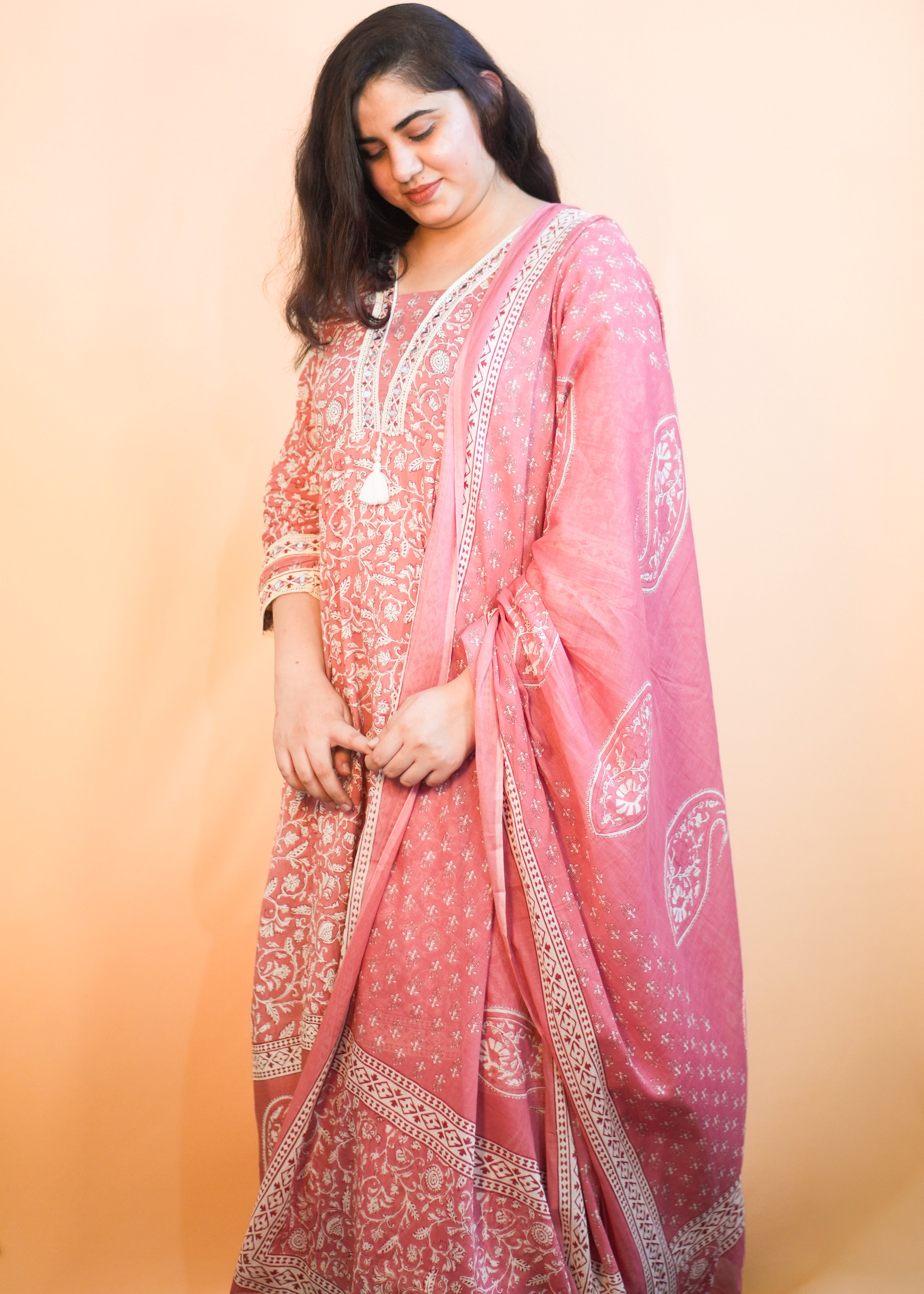 Woman wearing a pink traditional outfit with white patterns on a peach background