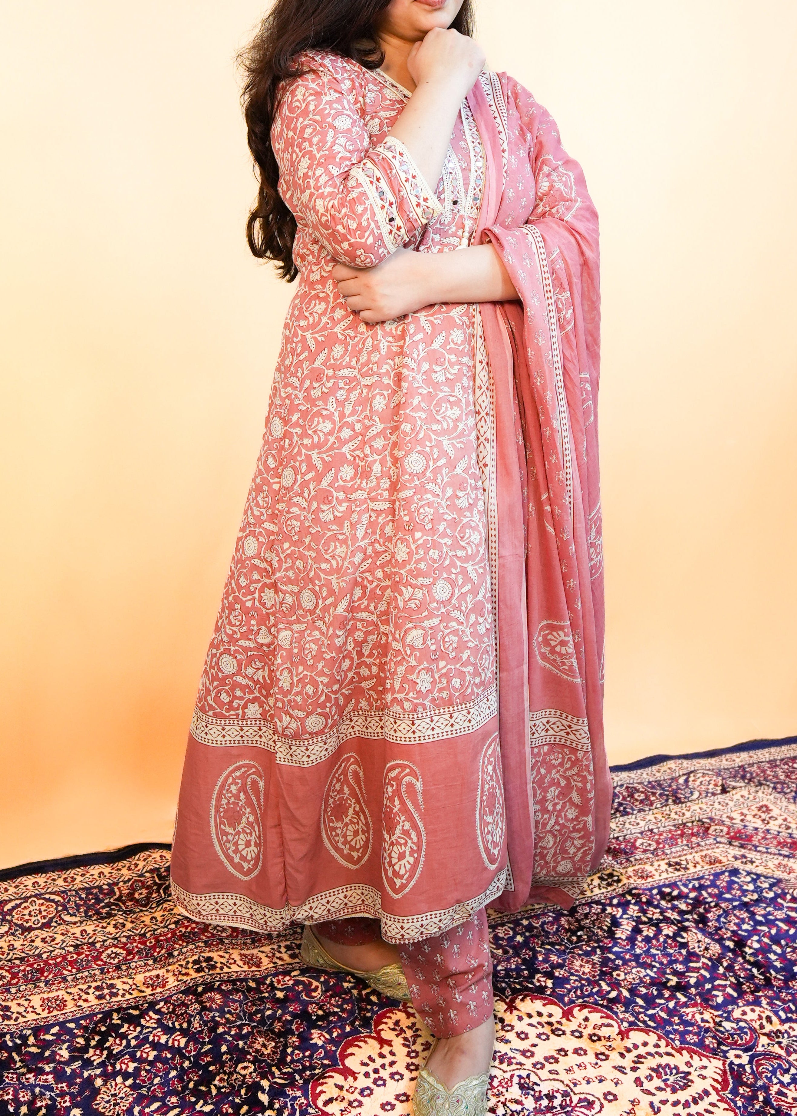Woman wearing a pink traditional outfit with a matching dupatta on a patterned carpet.