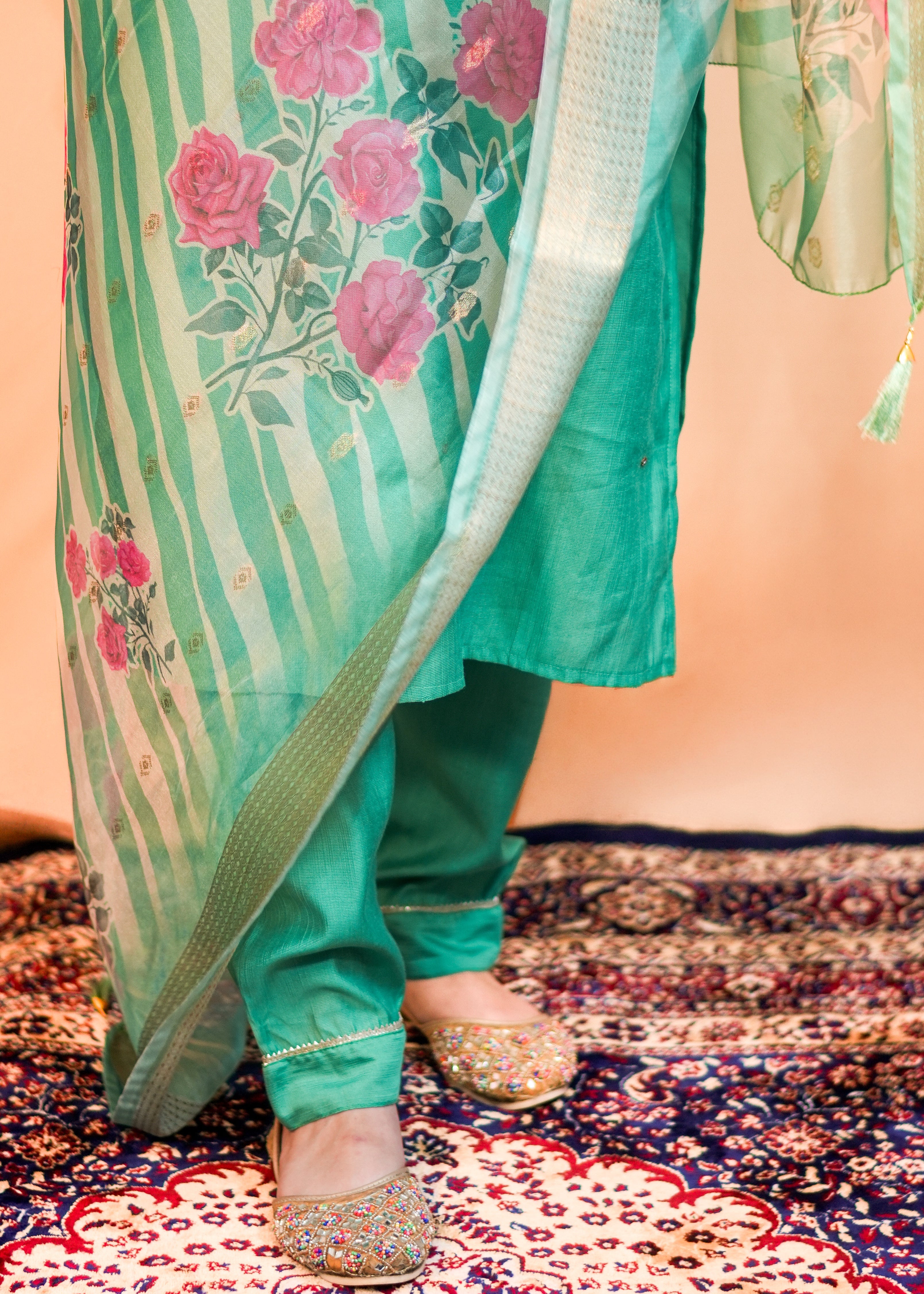 Person wearing a green traditional outfit with floral patterns on a patterned rug.