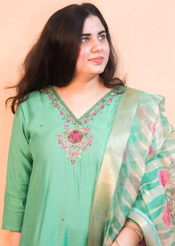 Woman wearing a green embroidered traditional outfit with a plain background
