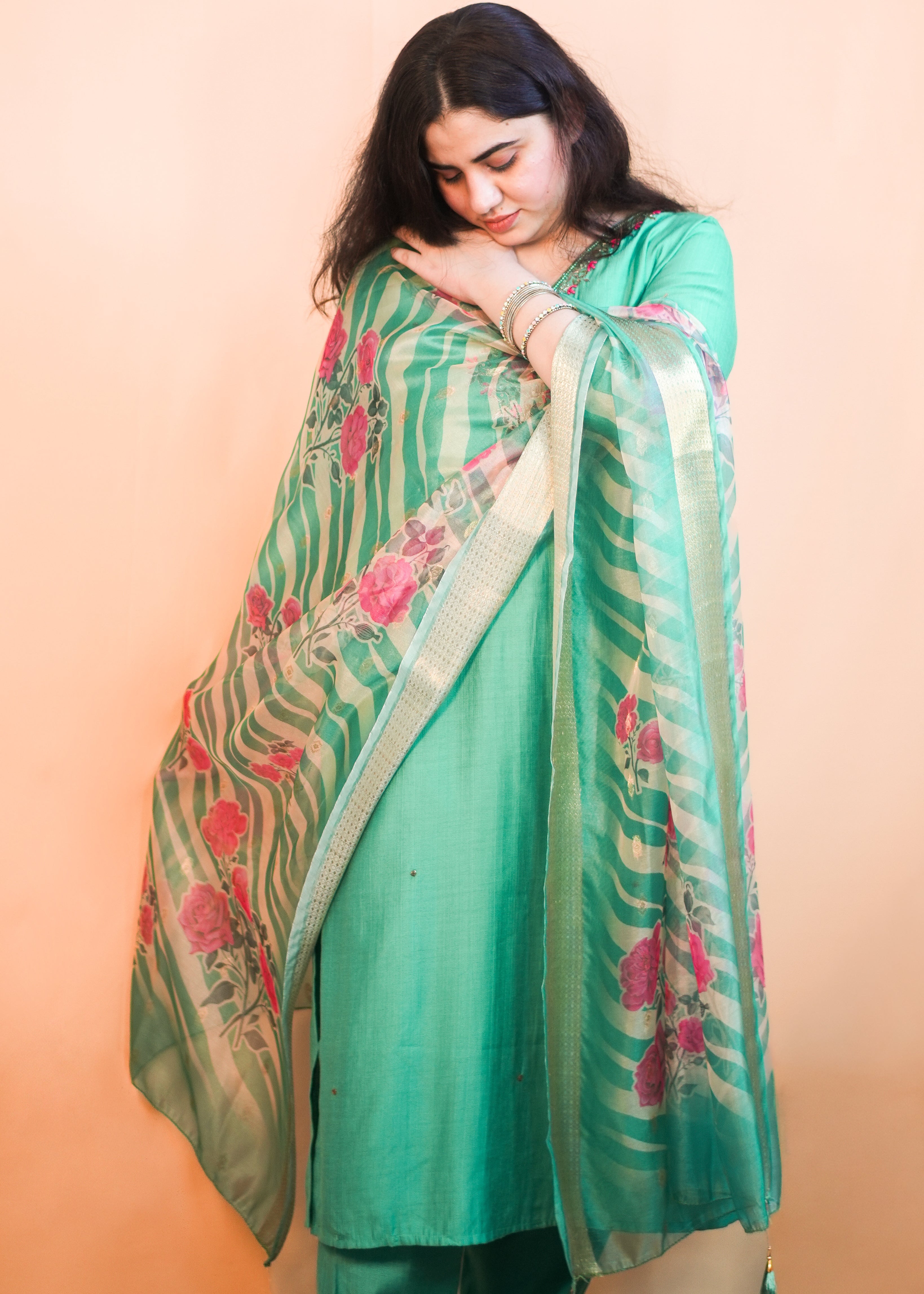 Woman wearing a green saree with floral patterns on a peach background