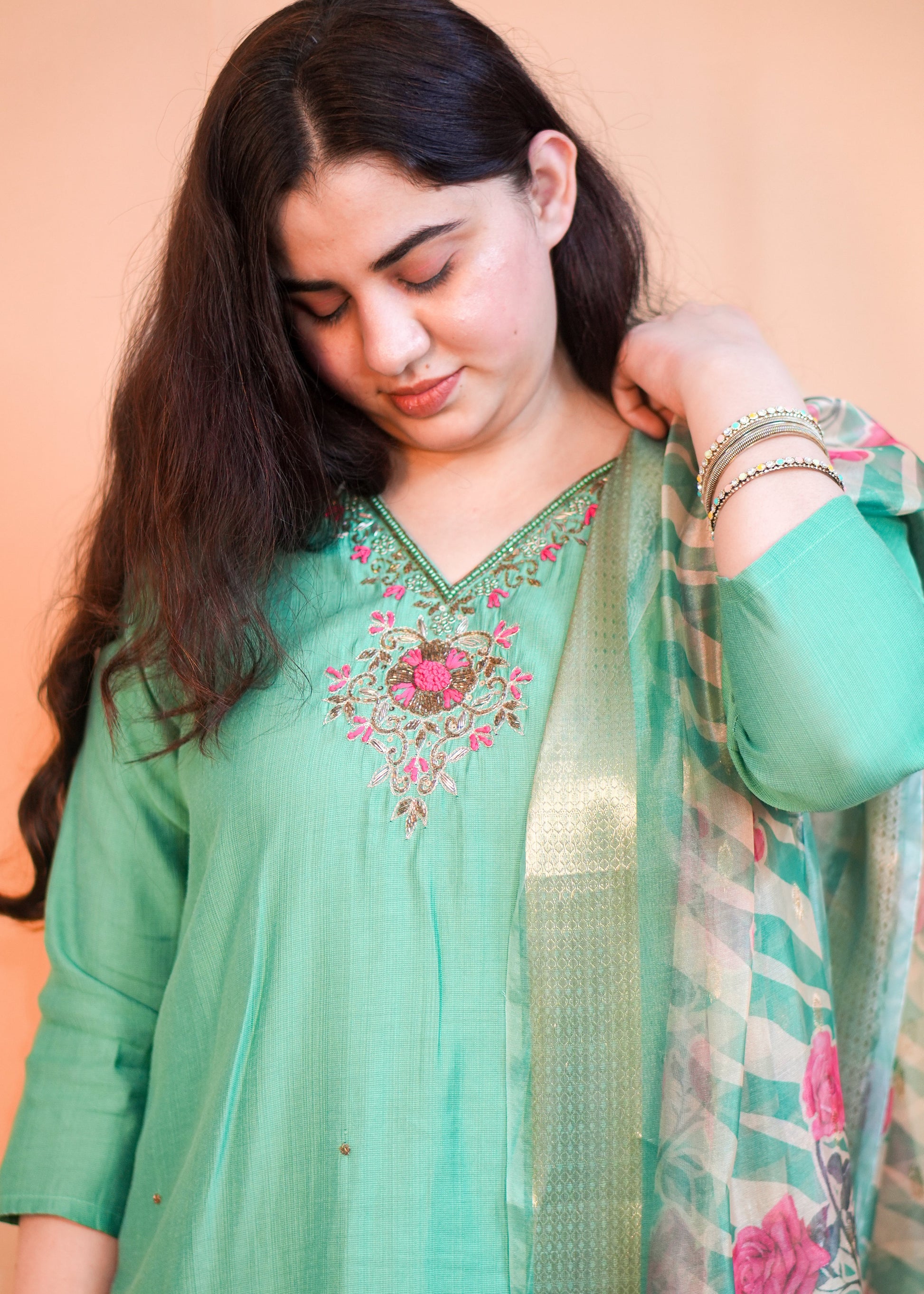 Woman wearing a green embroidered outfit with a plain background