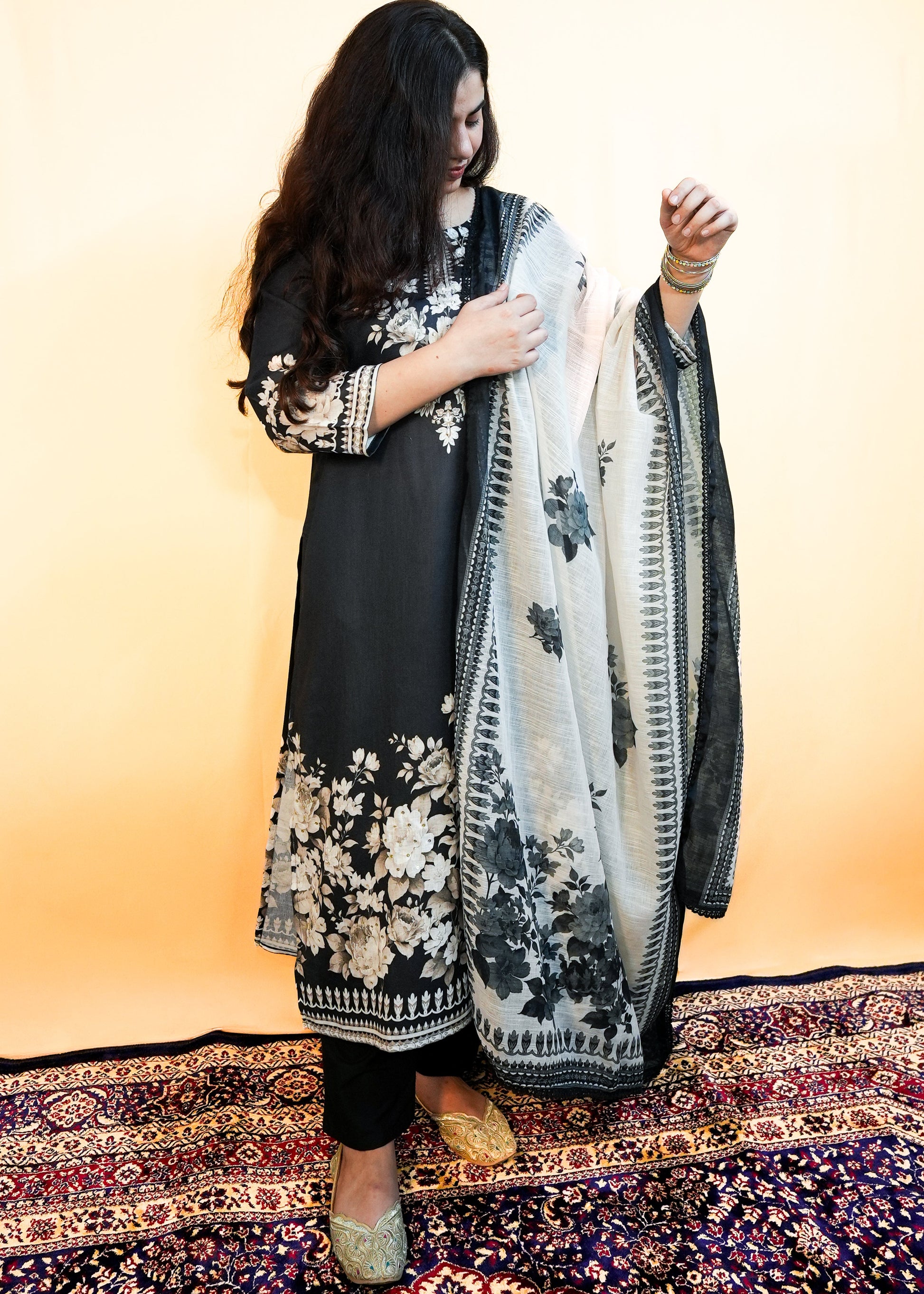 Woman holding a black and white floral scarf on a patterned rug with a yellow background
