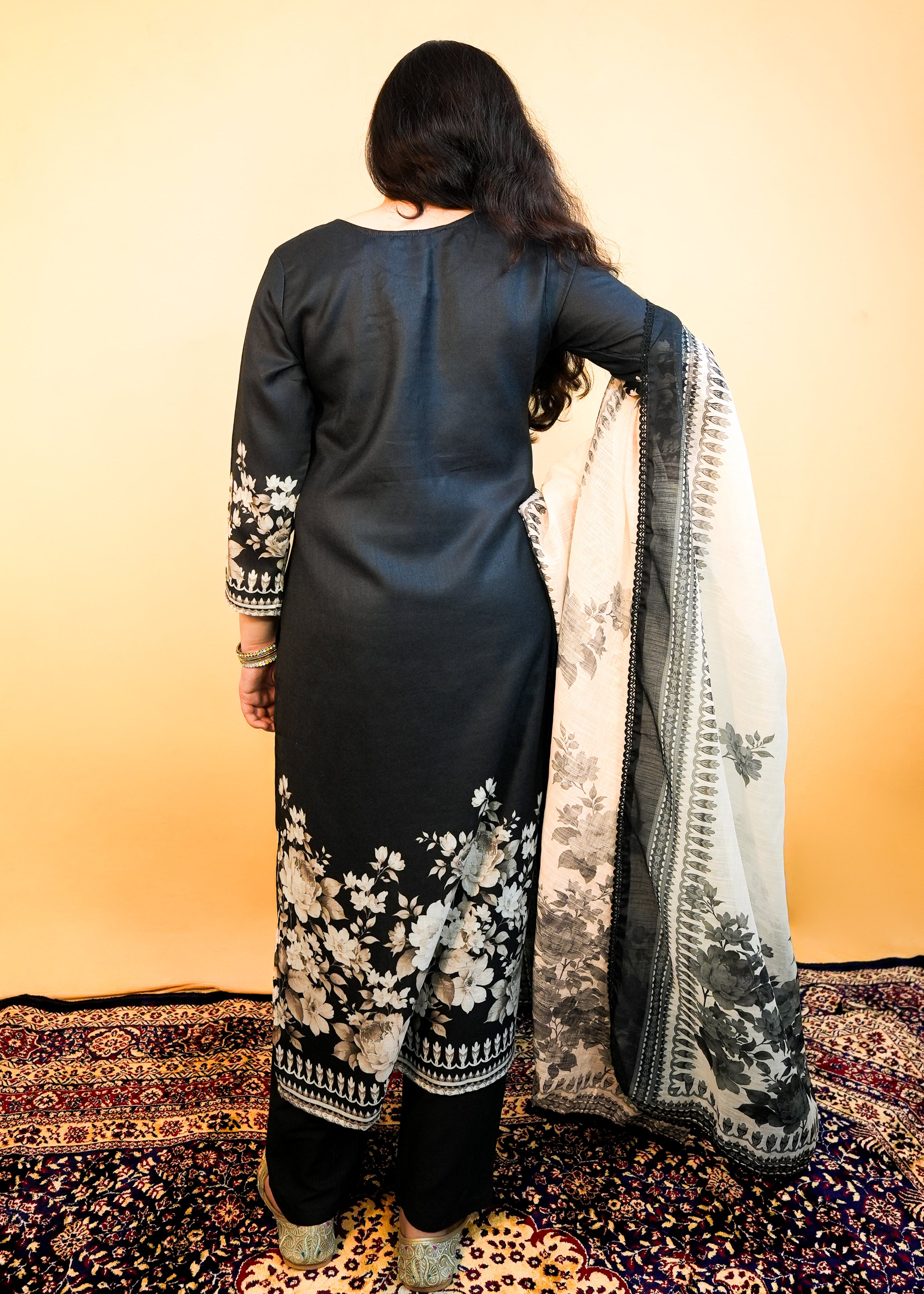 Woman holding a floral dupatta against a warm-toned wall.