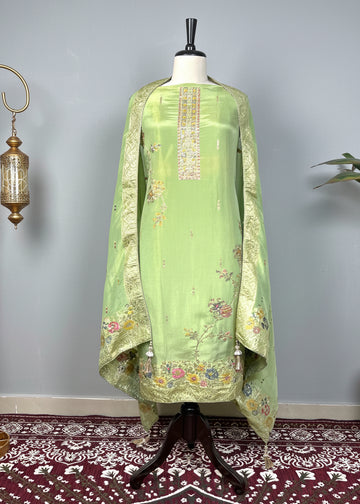 Green embroidered dress on a mannequin against a decorative wall with a patterned rug.